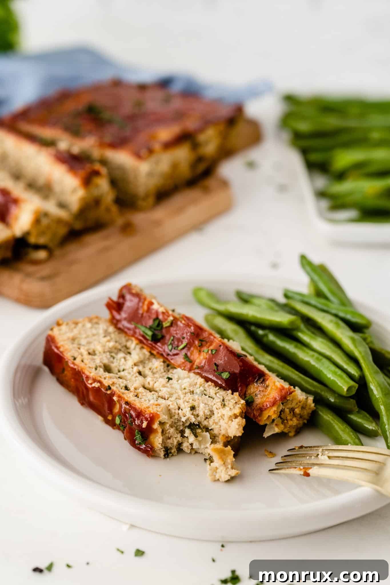Healthy chicken meatloaf slices served on a plate with roasted green beans, showcasing a complete meal.