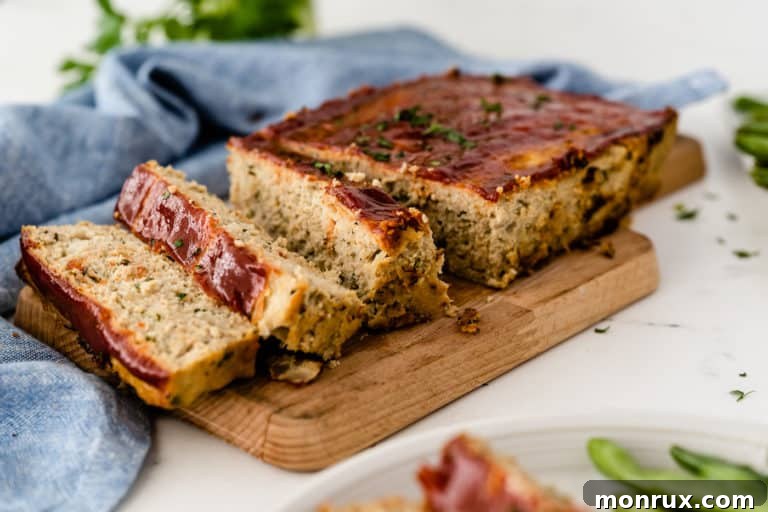 Cooked and sliced chicken meatloaf on a cutting board, garnished with fresh herbs, ready to be served.