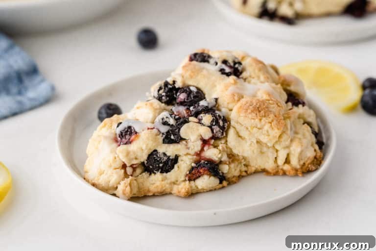 A delicious gluten-free blueberry scone, sliced in half, revealing its tender, moist interior with visible blueberries, topped with a delicate lemon glaze.