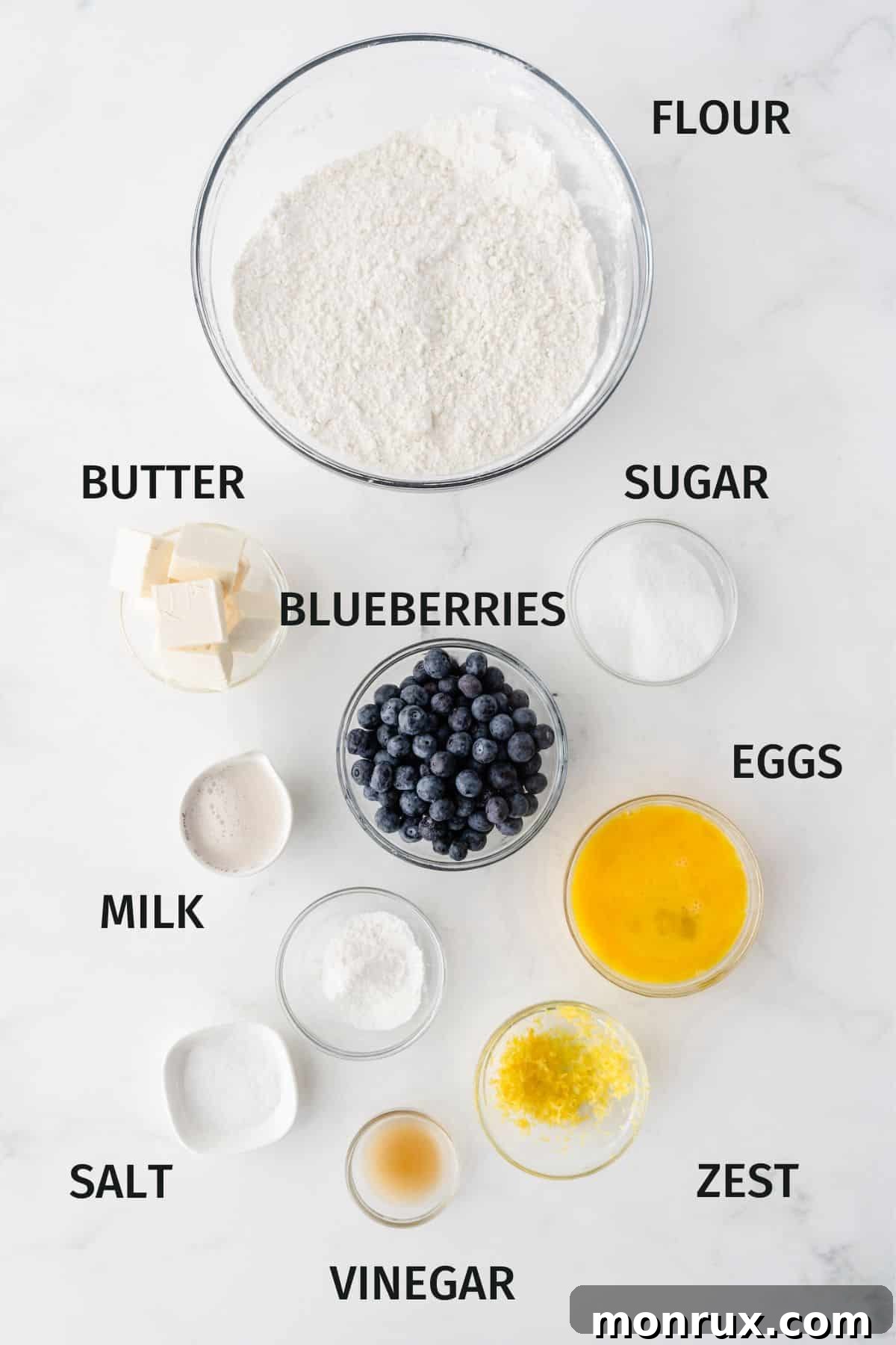 A beautifully composed flat lay of all the essential ingredients for gluten-free blueberry scones, clearly labeled and arranged, showcasing fresh blueberries, lemon, gluten-free flour, and cold vegan butter.