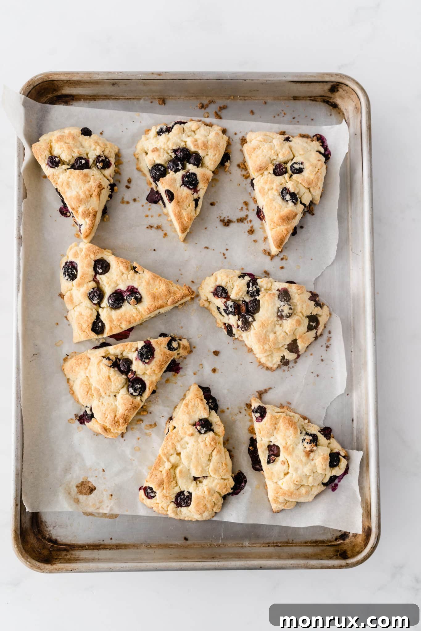 A warm baking sheet filled with freshly baked gluten-free blueberry scones, golden brown and ready to be glazed.