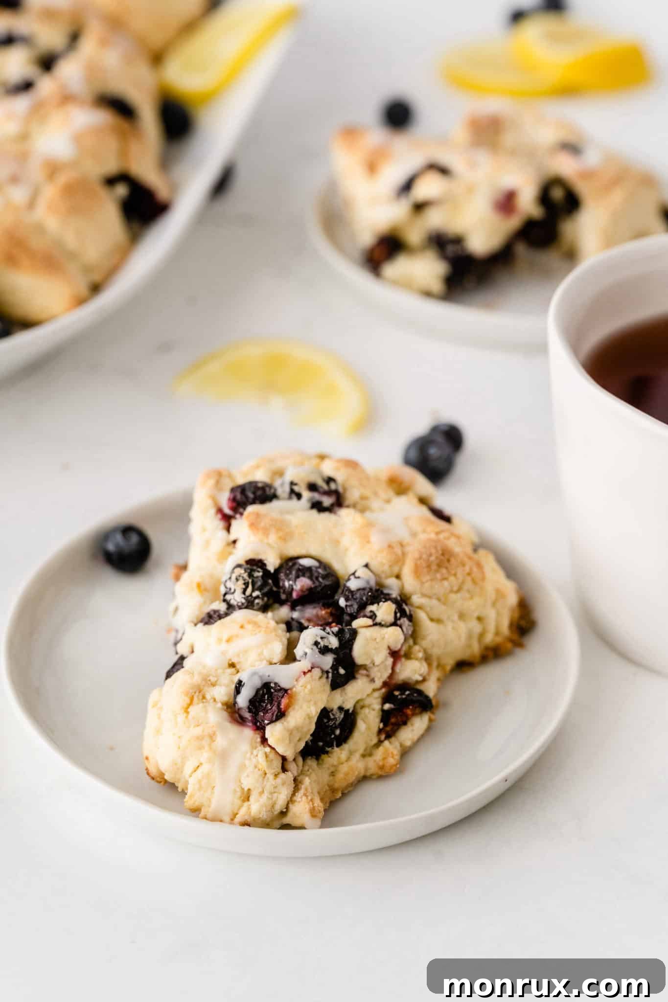 A rustic setting featuring a freshly baked gluten-free blueberry scone on a small white plate, adorned with a few fresh blueberries, accompanied by a steaming cup of tea – the perfect cozy moment.