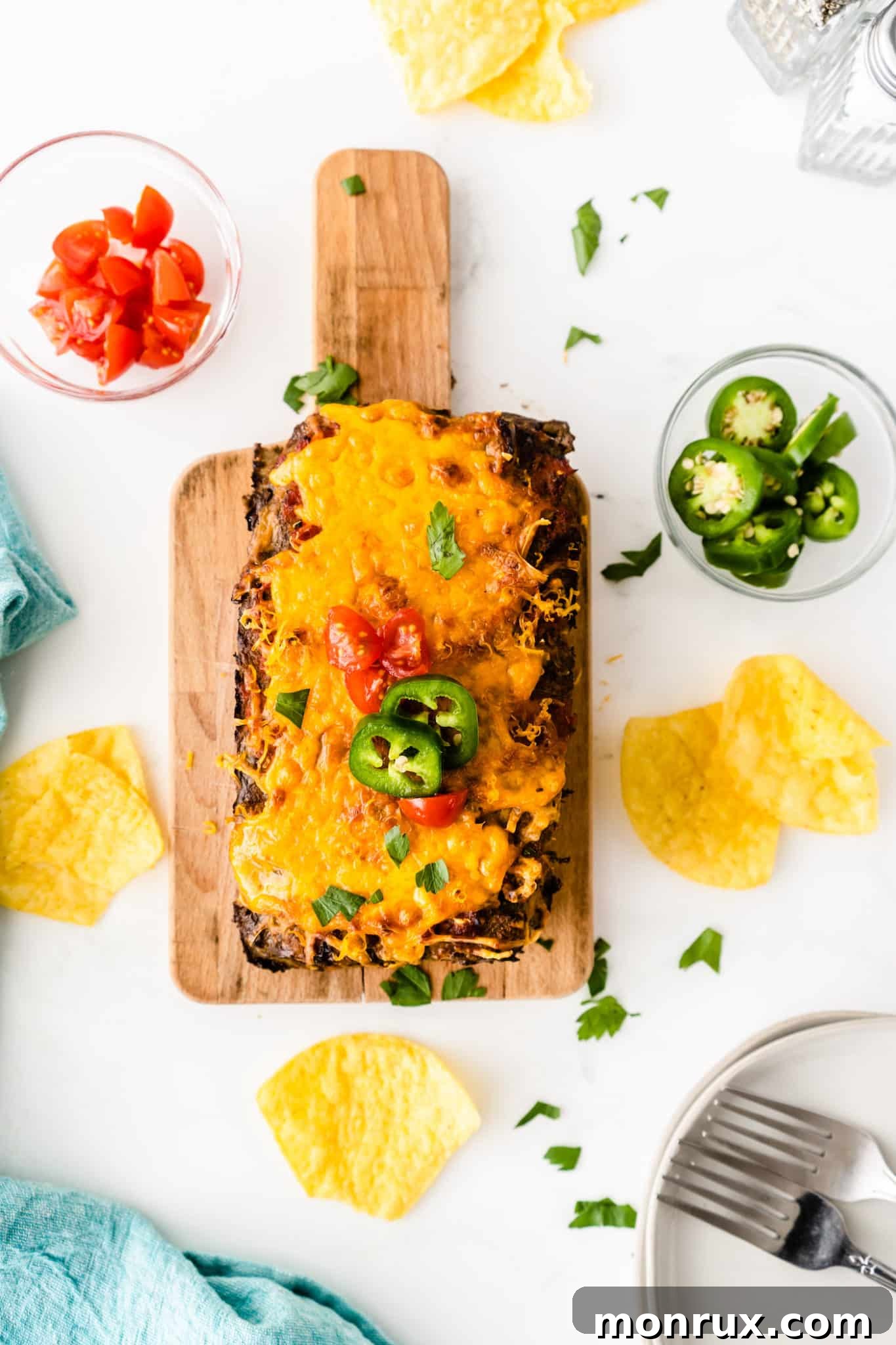 Cooked taco meatloaf served on a wooden cutting board with extra toppings like fresh cilantro and lime wedges.