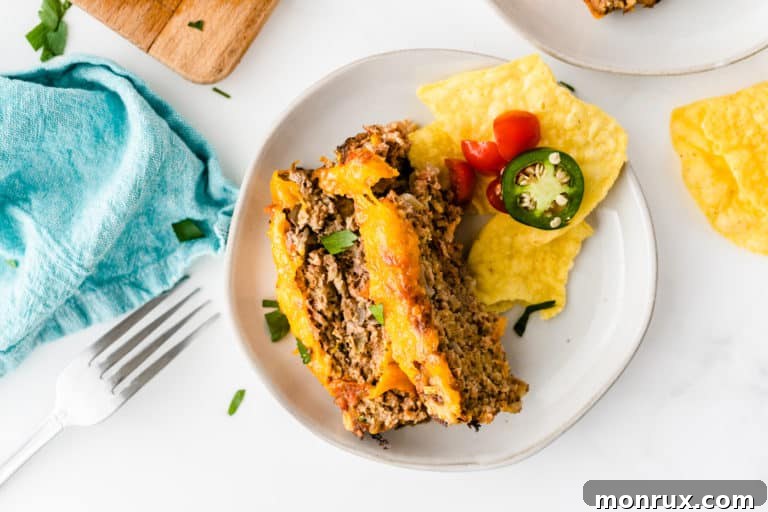 White plate with two servings of sliced taco meatloaf with a side of tortilla chips and fresh toppings