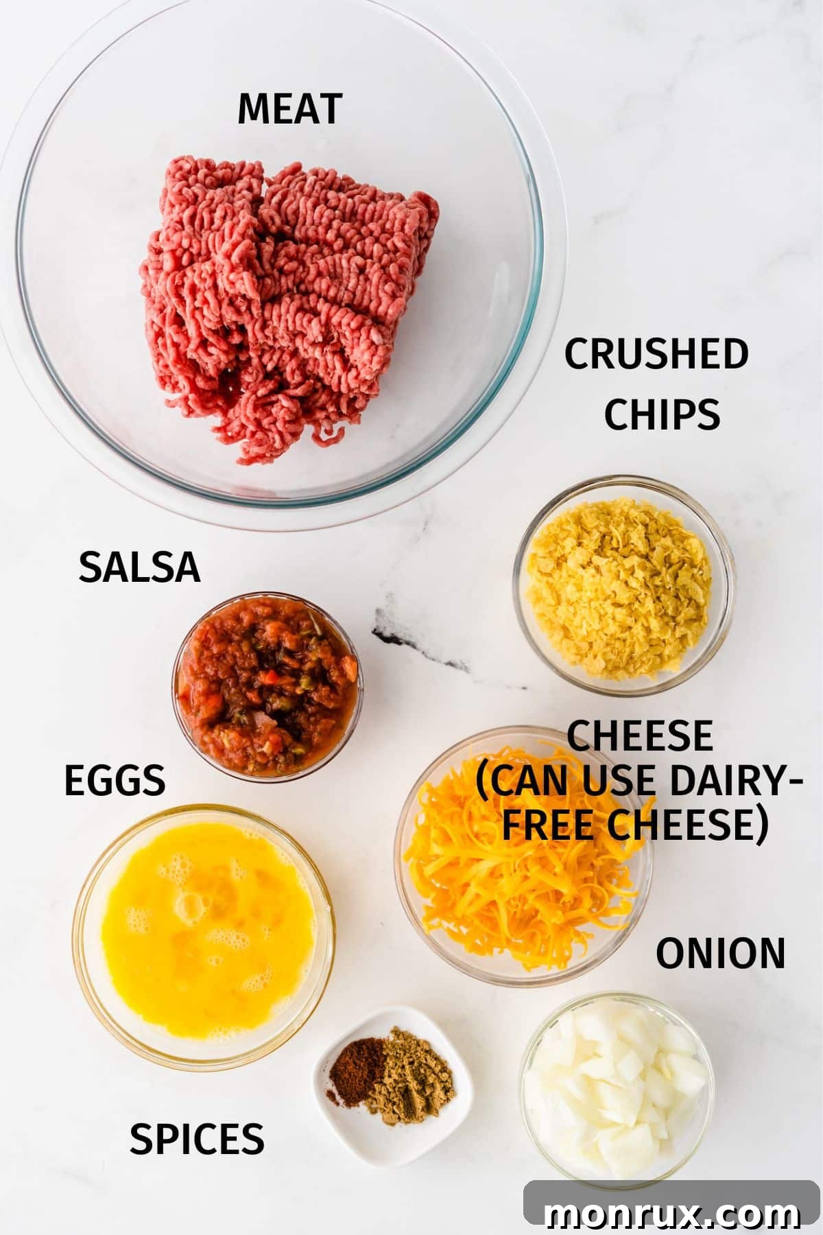 Photo with labeled fresh ingredients for taco meatloaf recipe including ground beef, salsa, tortilla chips, and onion.