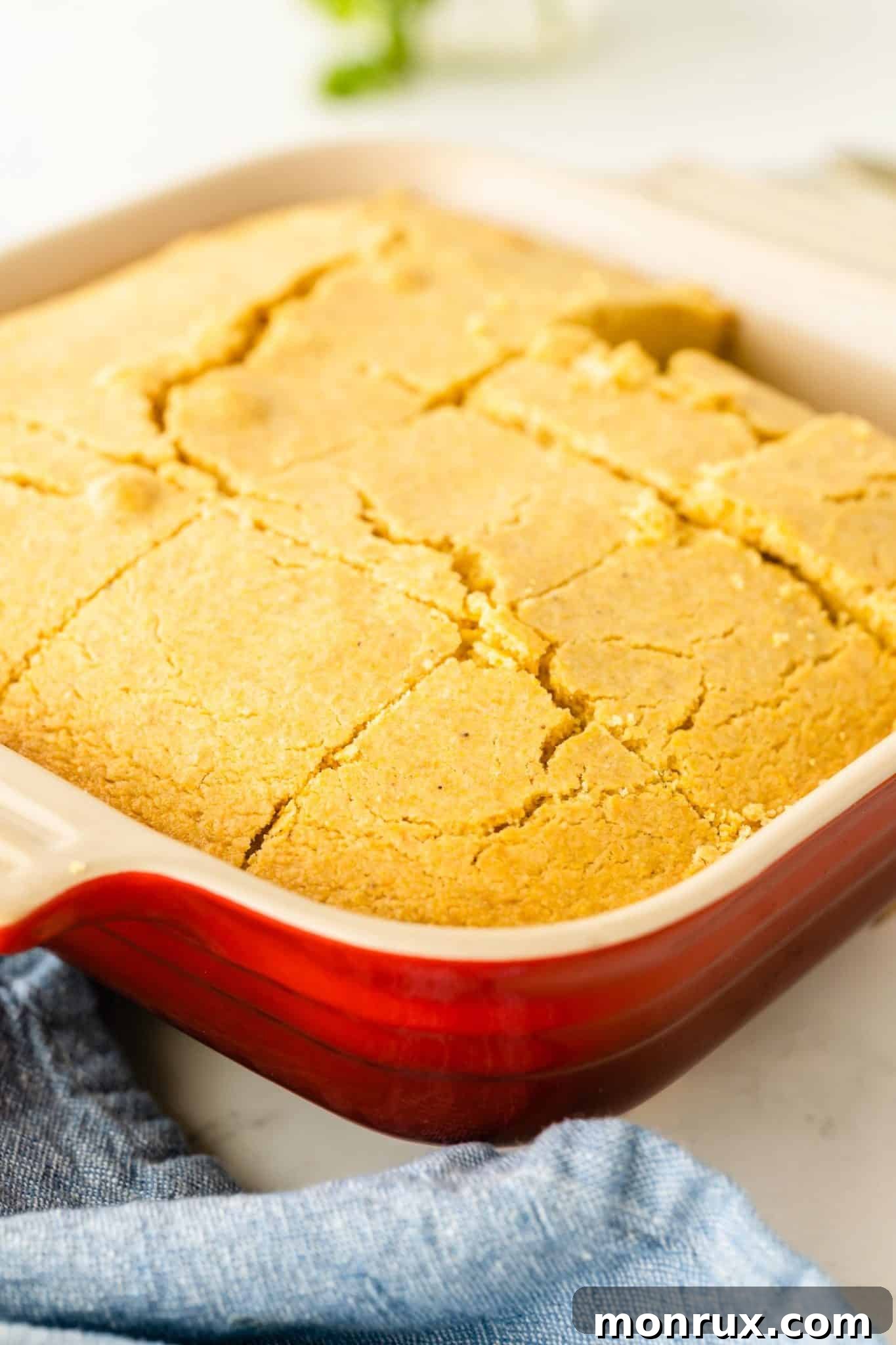 A close-up shot of a golden-brown gluten-free dairy-free cornbread in a pan, with a slice already removed, highlighting its moist texture.