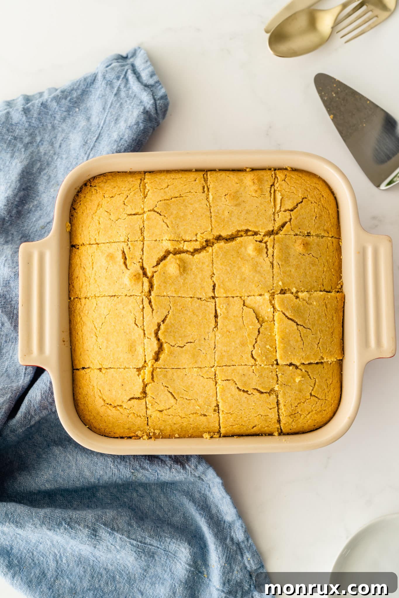 Freshly baked gluten-free dairy-free cornbread cooling in a square baking dish on a kitchen countertop, ready to be sliced.