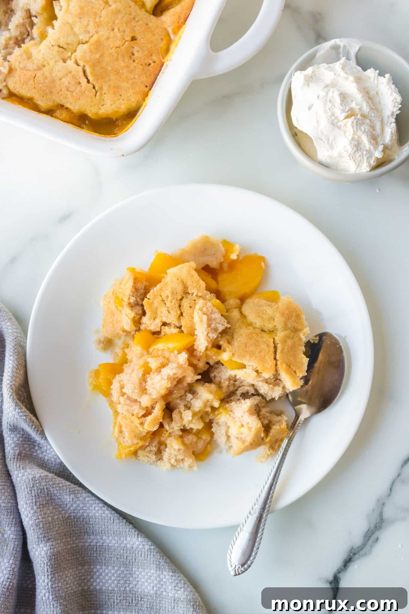 A plate of golden-brown peach cobbler made with almond flour, served with a spoon and a napkin.