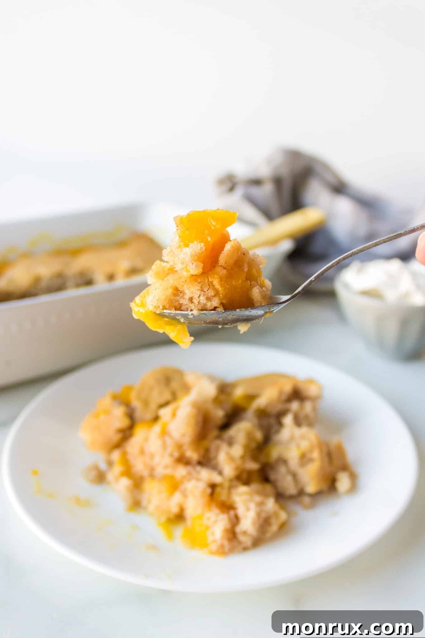 A spoonful of almond flour peach cobbler with a dollop of whipped cream, ready to eat.
