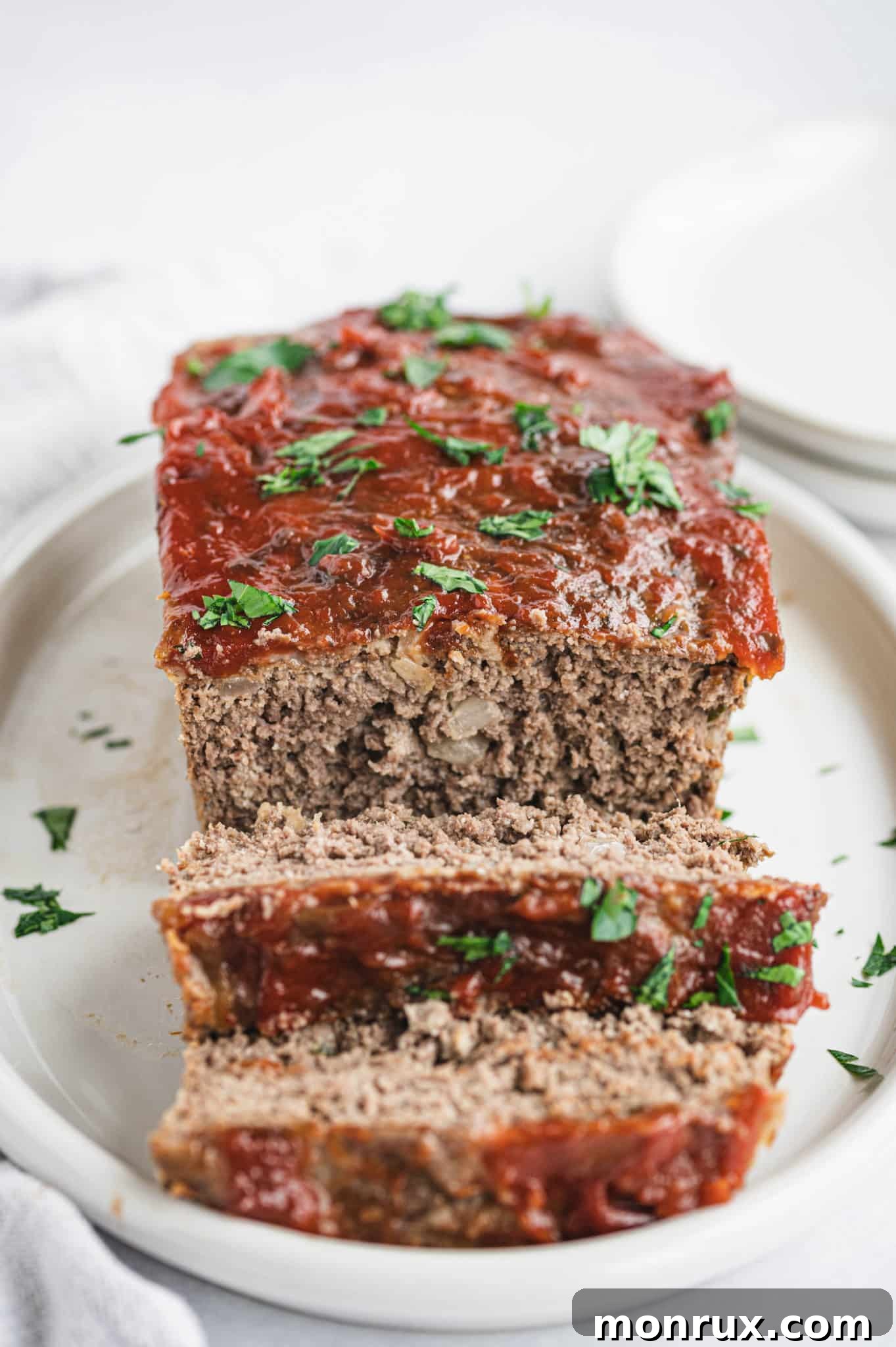Sliced meatloaf made without breadcrumbs served on a plate, garnished with fresh herbs.