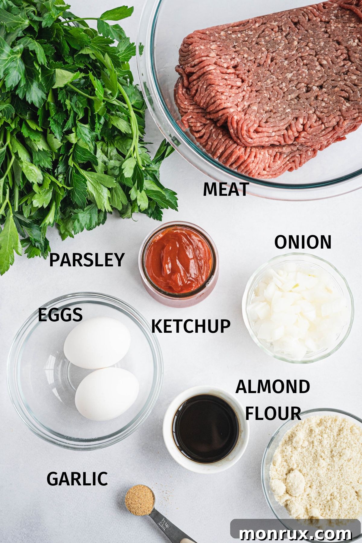 Photo with labeled ingredients for gluten free meatloaf with almond flour, including ground beef, almond flour, eggs, onion, garlic, parsley, and ketchup.