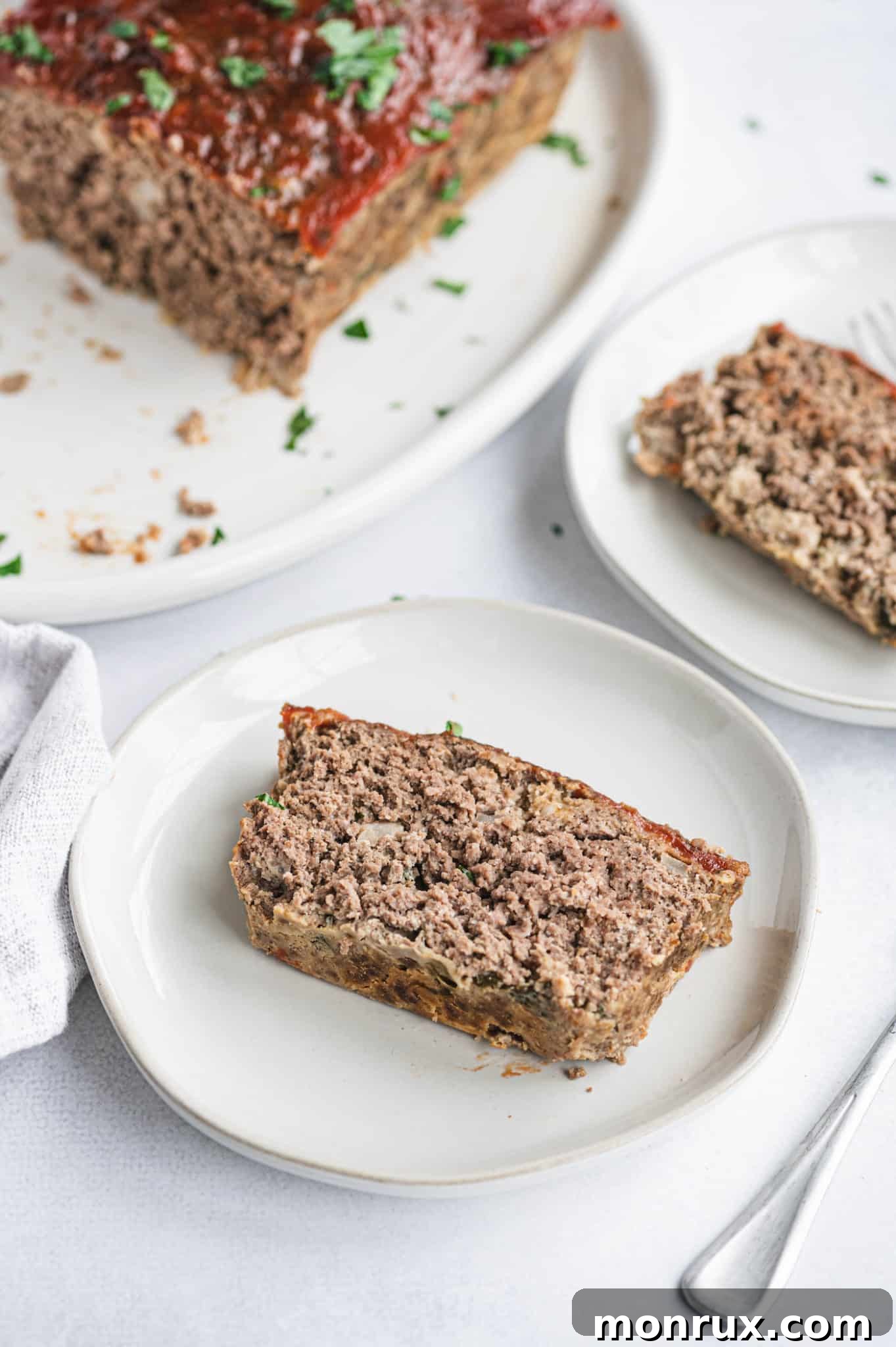 A perfectly sliced portion of gluten-free meatloaf on a white plate with fresh garnish.