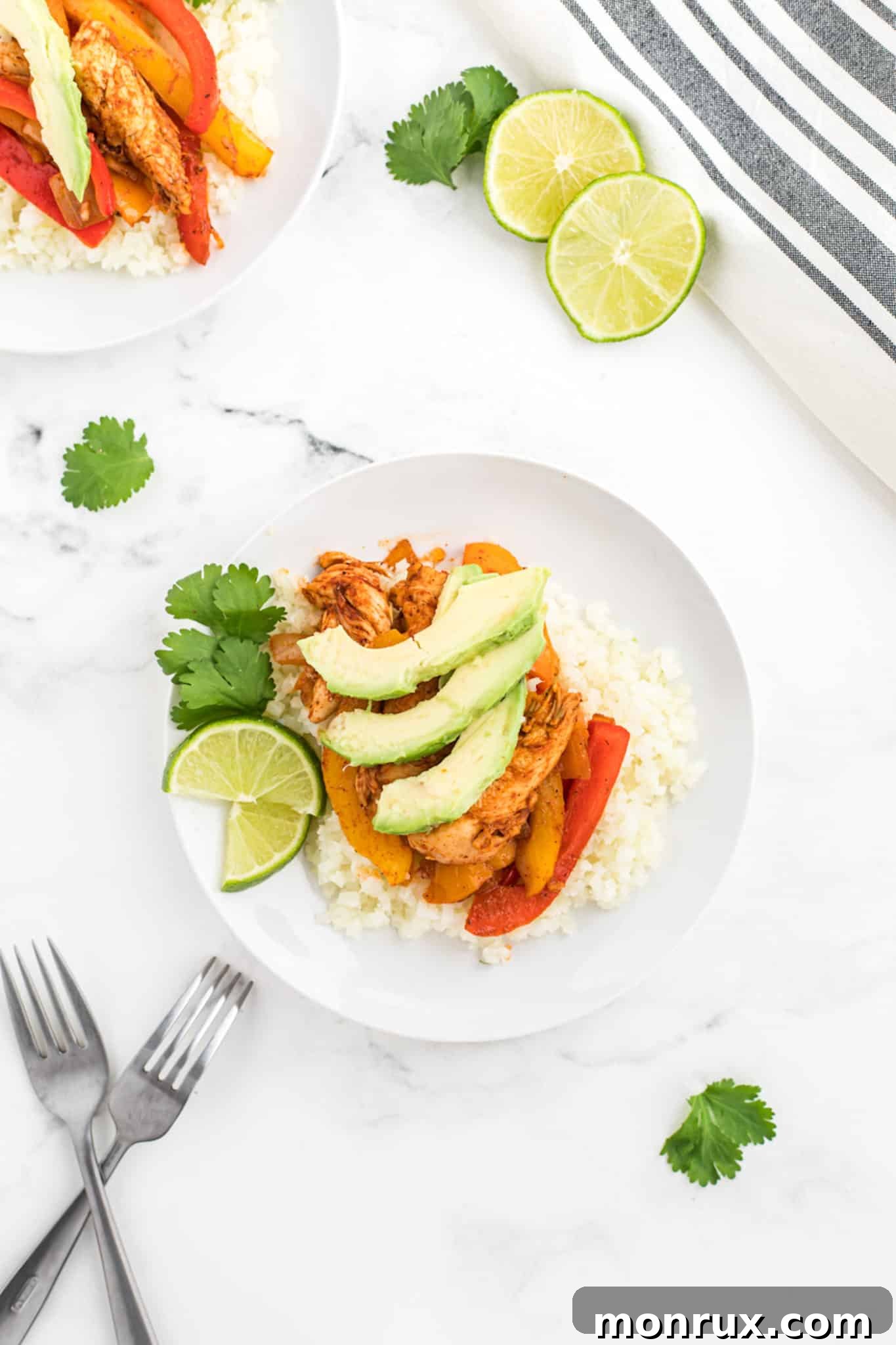 Keto chicken fajitas topped with avocado slices served over cauliflower rice in a bowl.