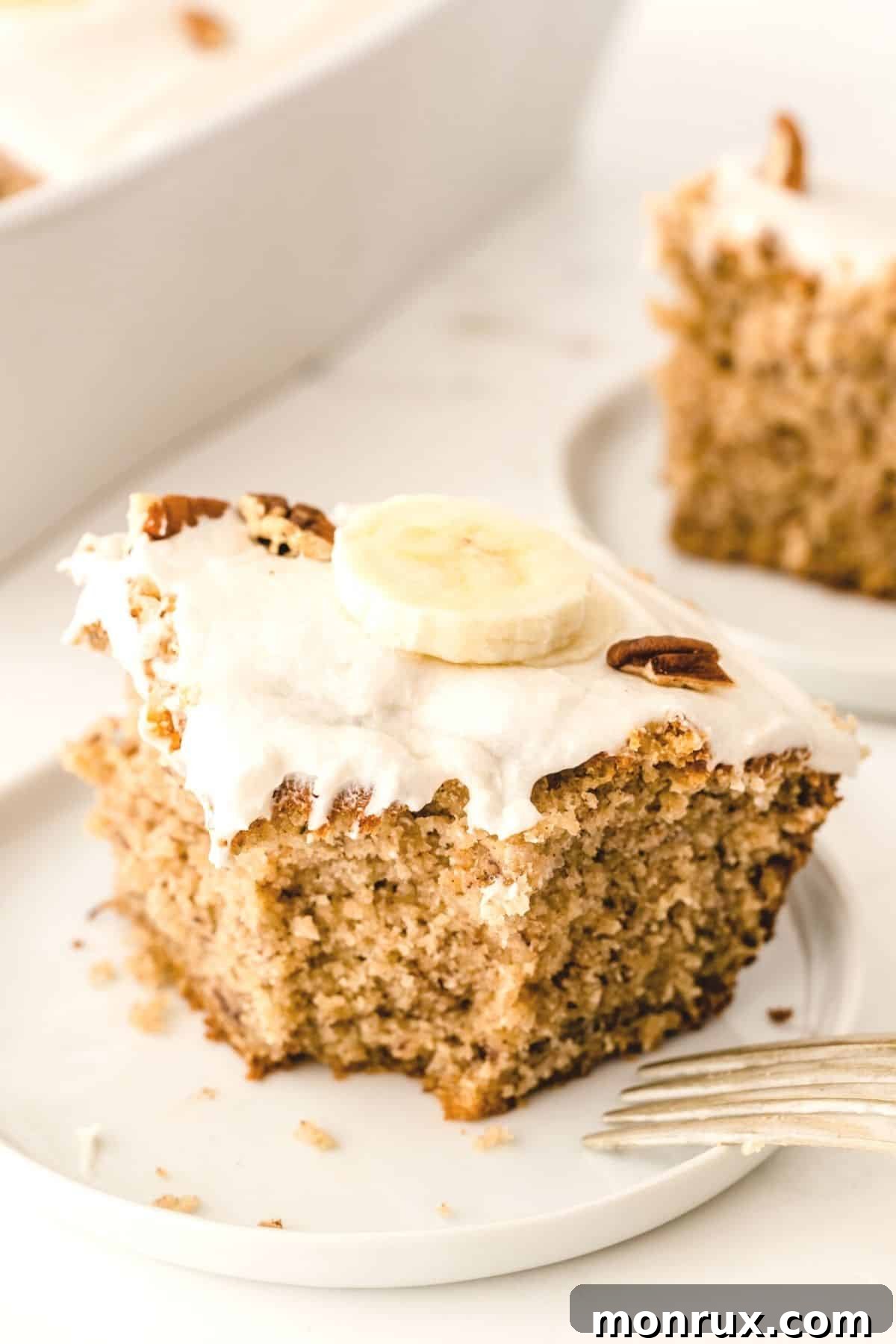 A slice of moist gluten-free and dairy-free banana cake topped with creamy vanilla frosting and a fork on a white plate, ready to be enjoyed.