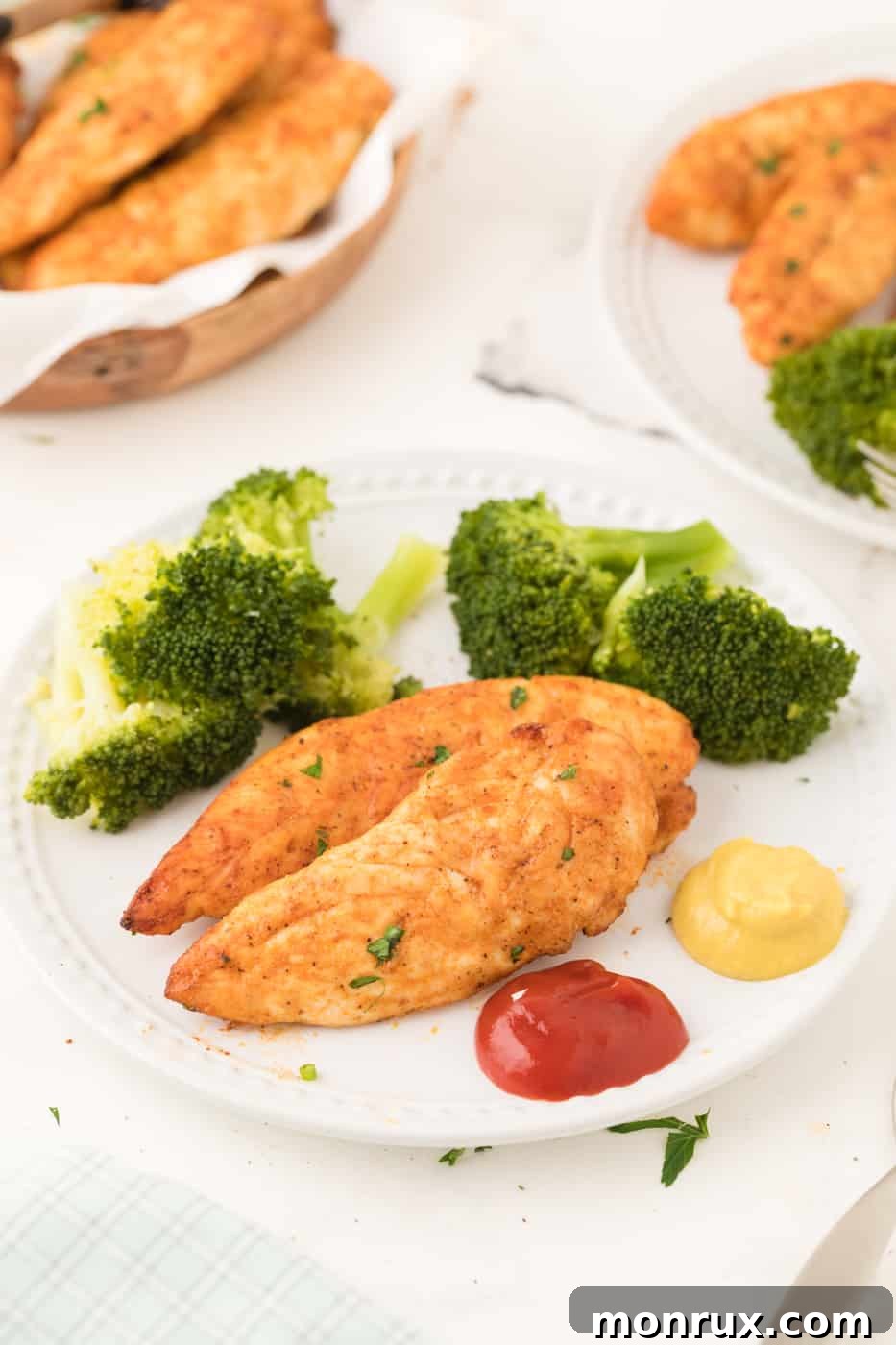 A plate of golden-brown air fryer chicken tenders served alongside fresh steamed broccoli florets.