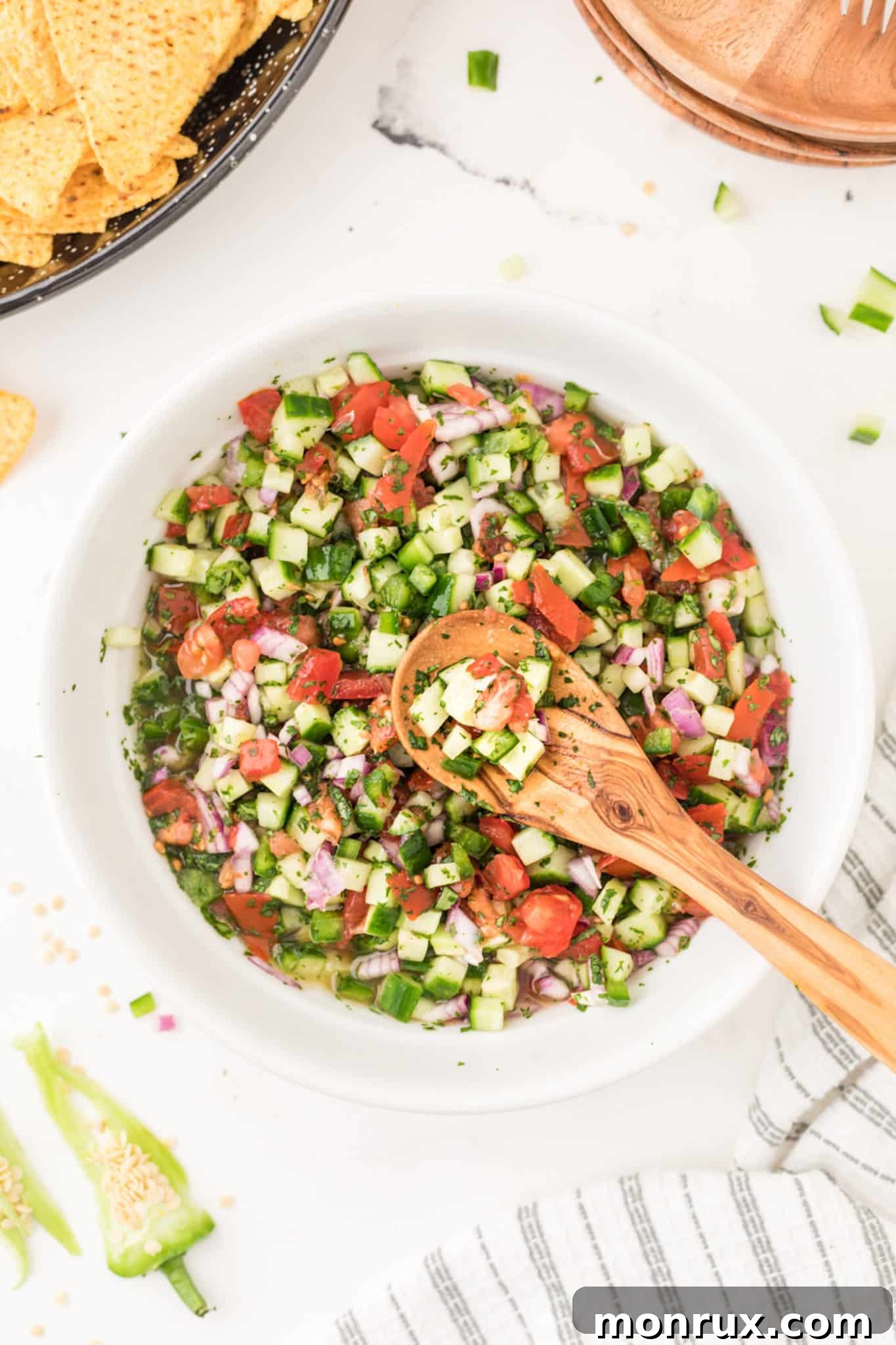 bowl of salsa with a wooden spoon on table, featuring fresh cucumber pico de gallo