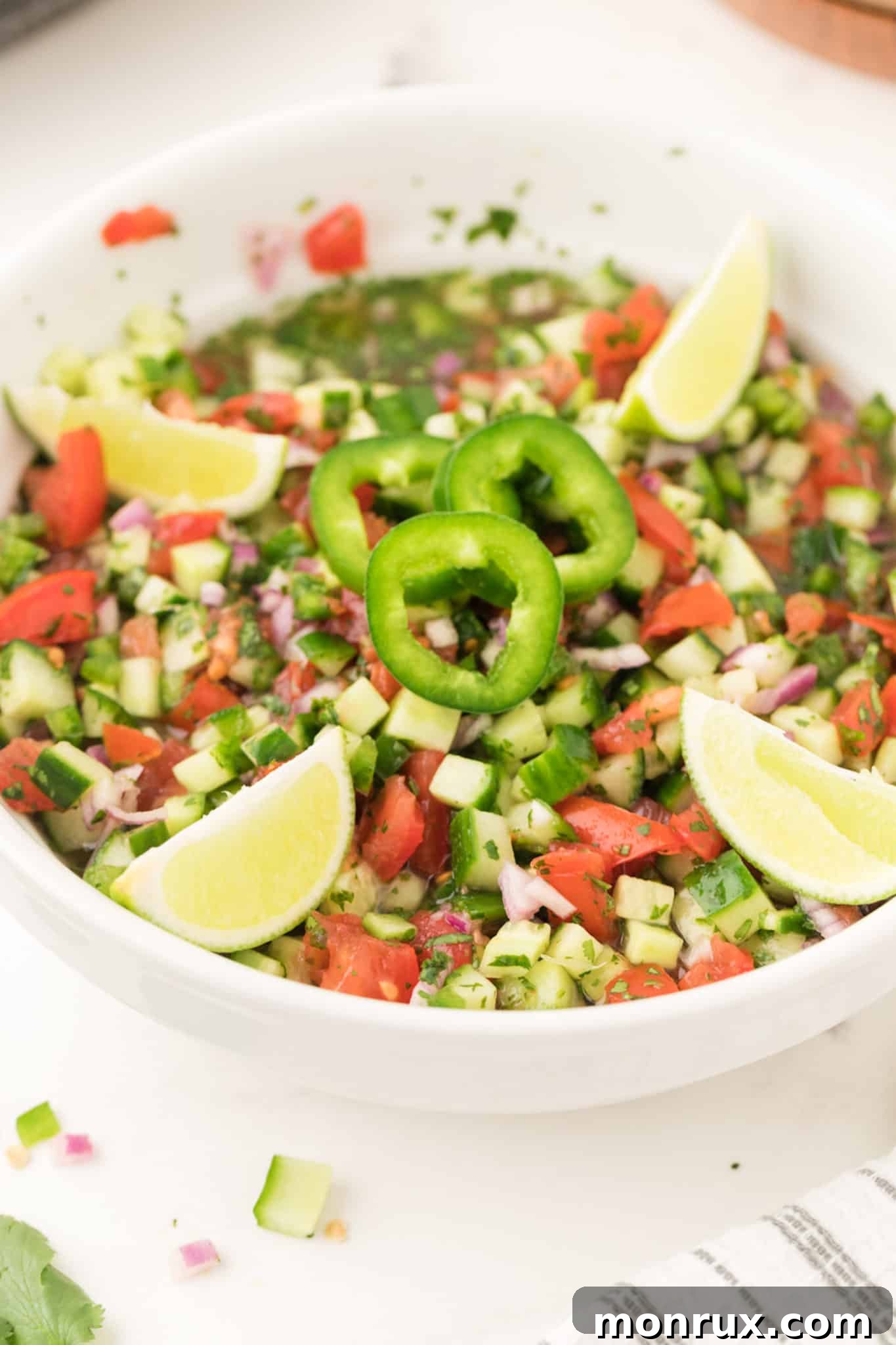 A large bowl of cucumber pico de gallo with whole jalapenos for garnish