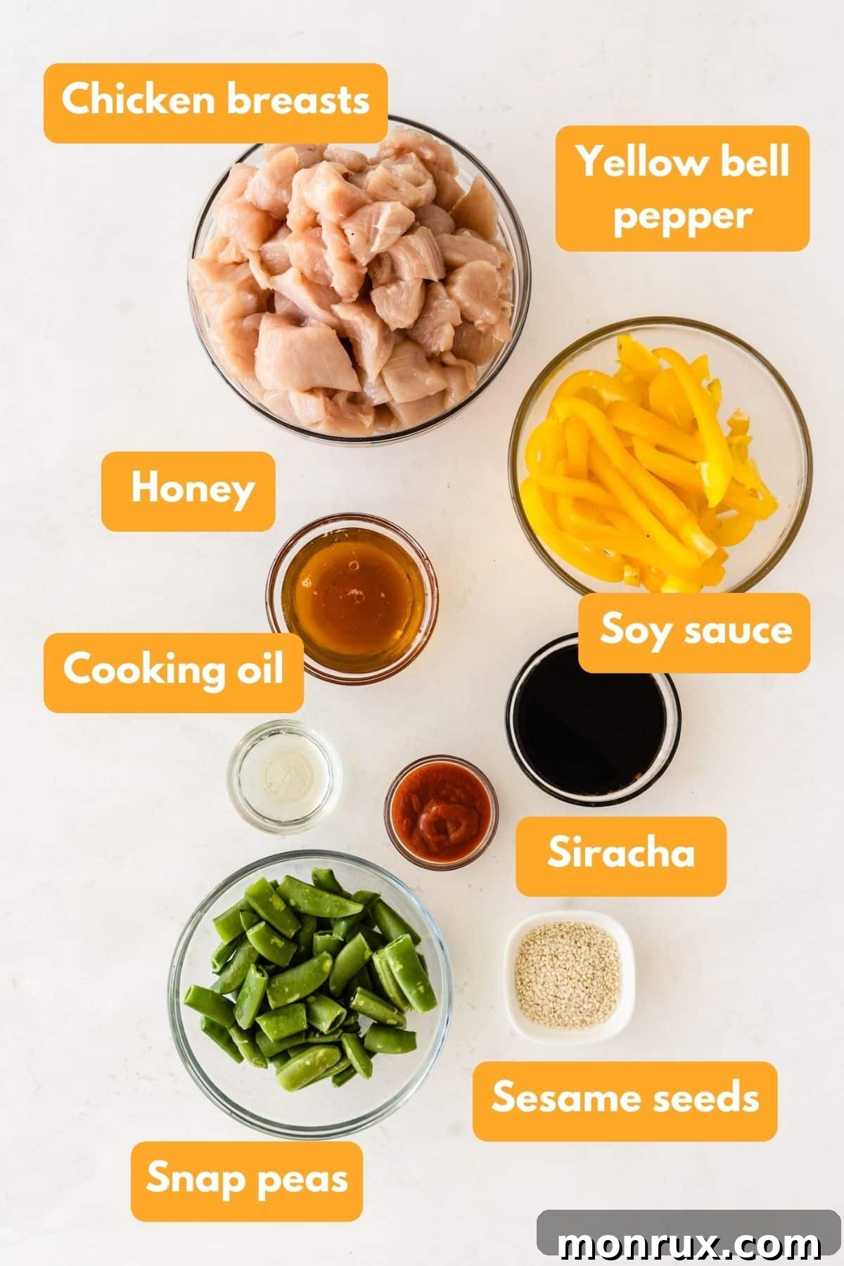 A collection of fresh ingredients laid out on a countertop, including chicken breasts, bell peppers, snap peas, honey, soy sauce, and sriracha, ready for making honey sesame chicken.