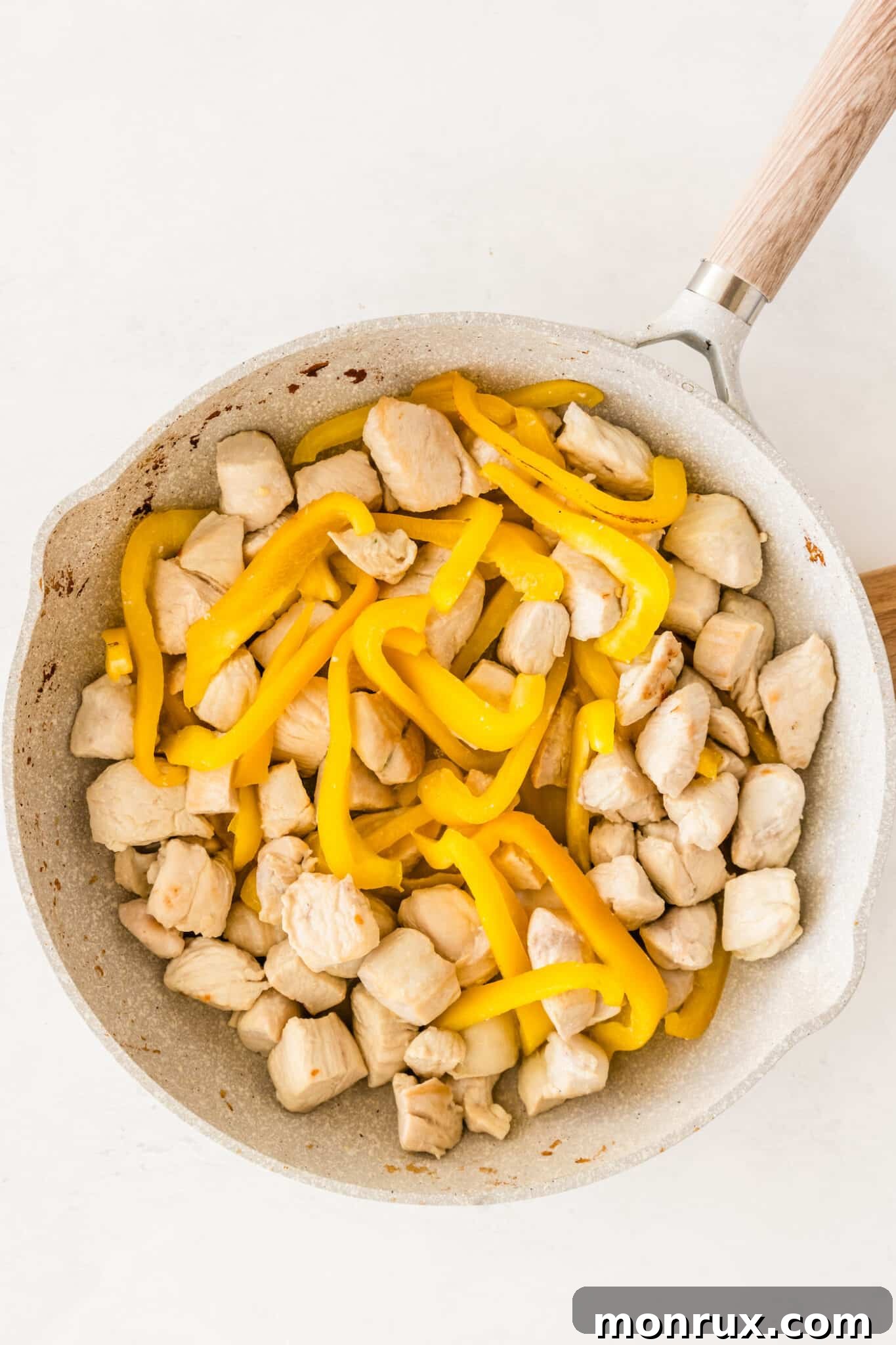 Diced chicken and sliced bell peppers being stir-fried in a hot nonstick skillet with oil.