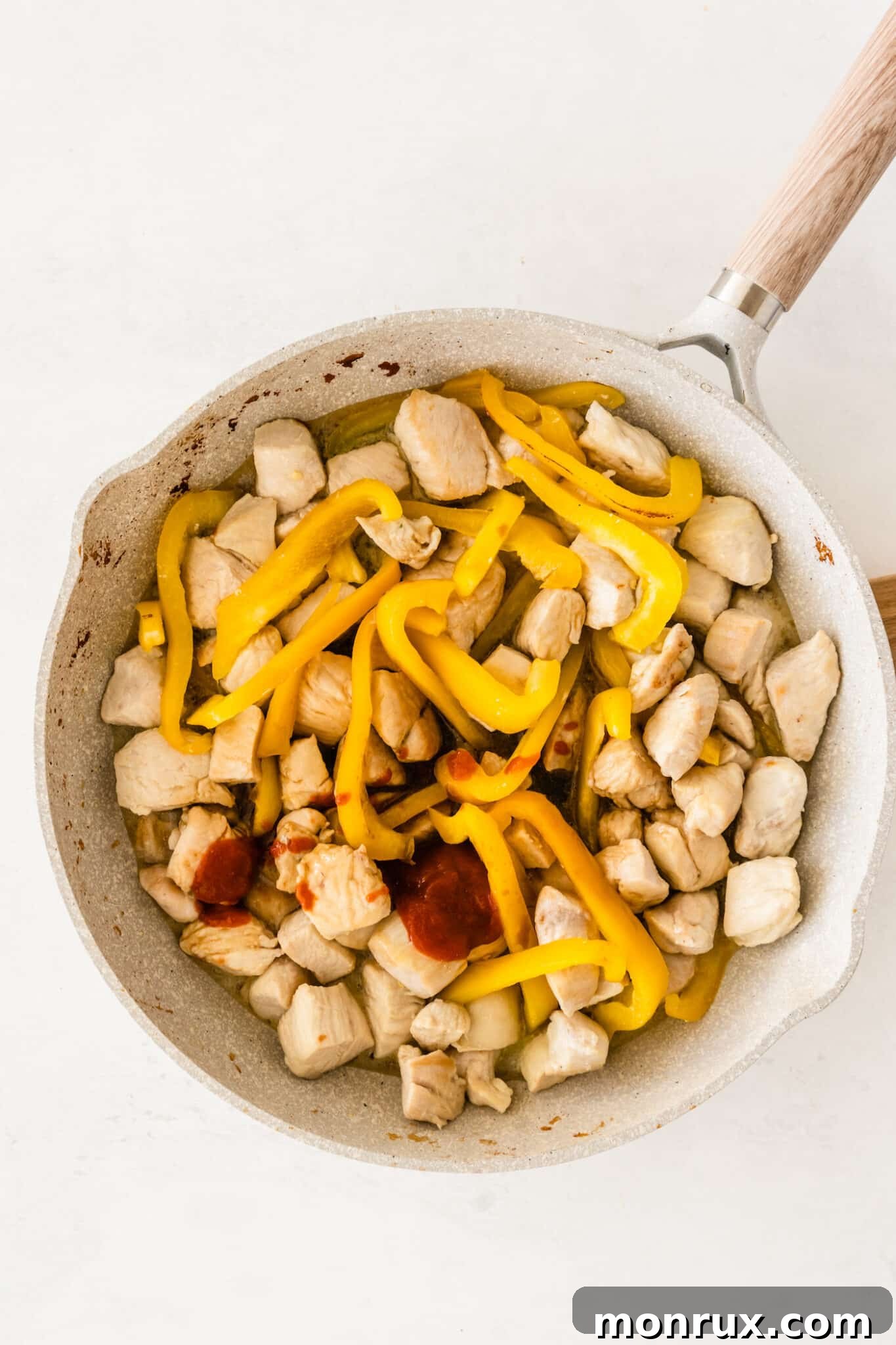 The cooking chicken and bell peppers in the pan, with honey and soy sauce being poured in, ready to form the sweet and savory sauce.