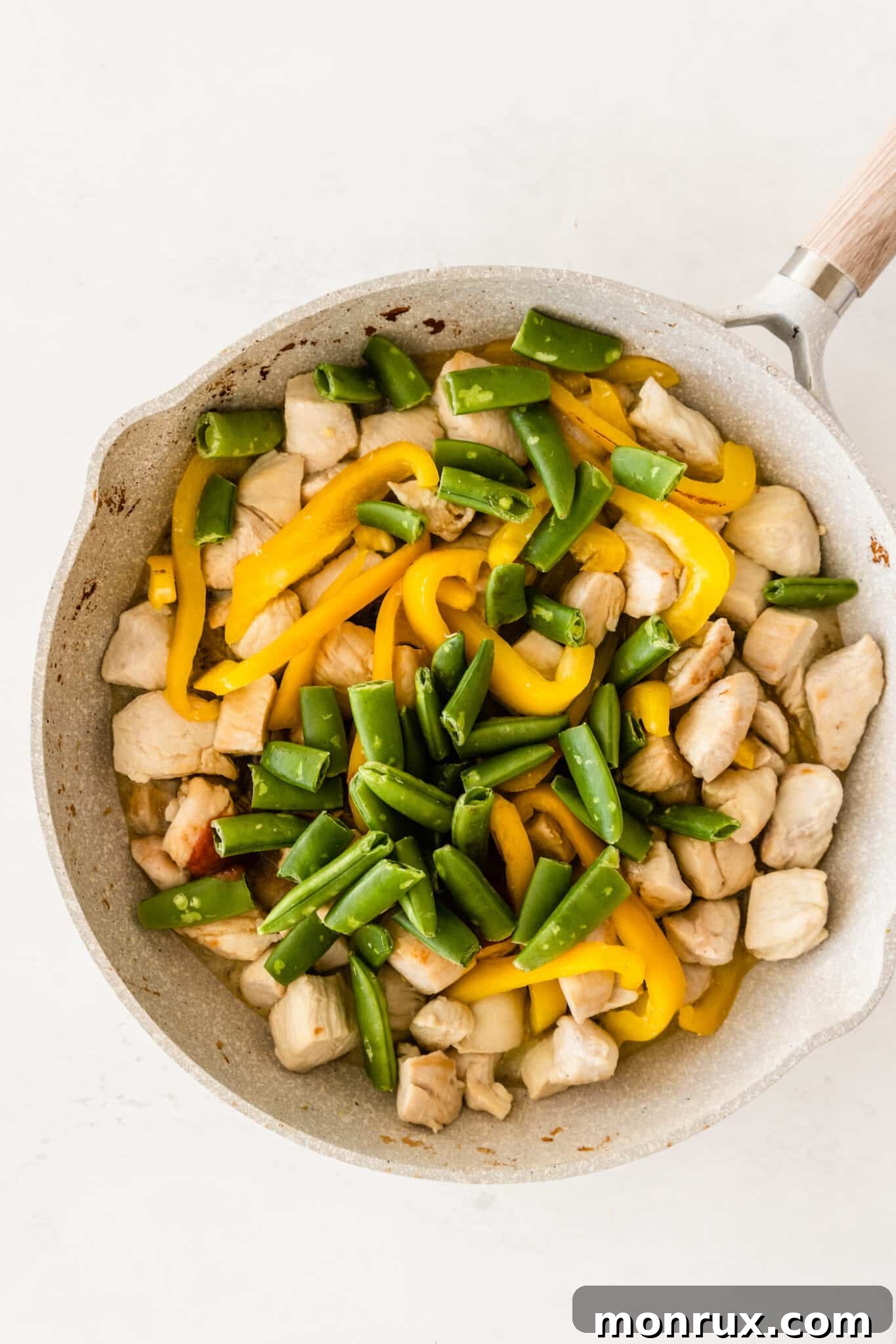 Snap peas added to the skillet with chicken, bell peppers, and sauce, simmering together.