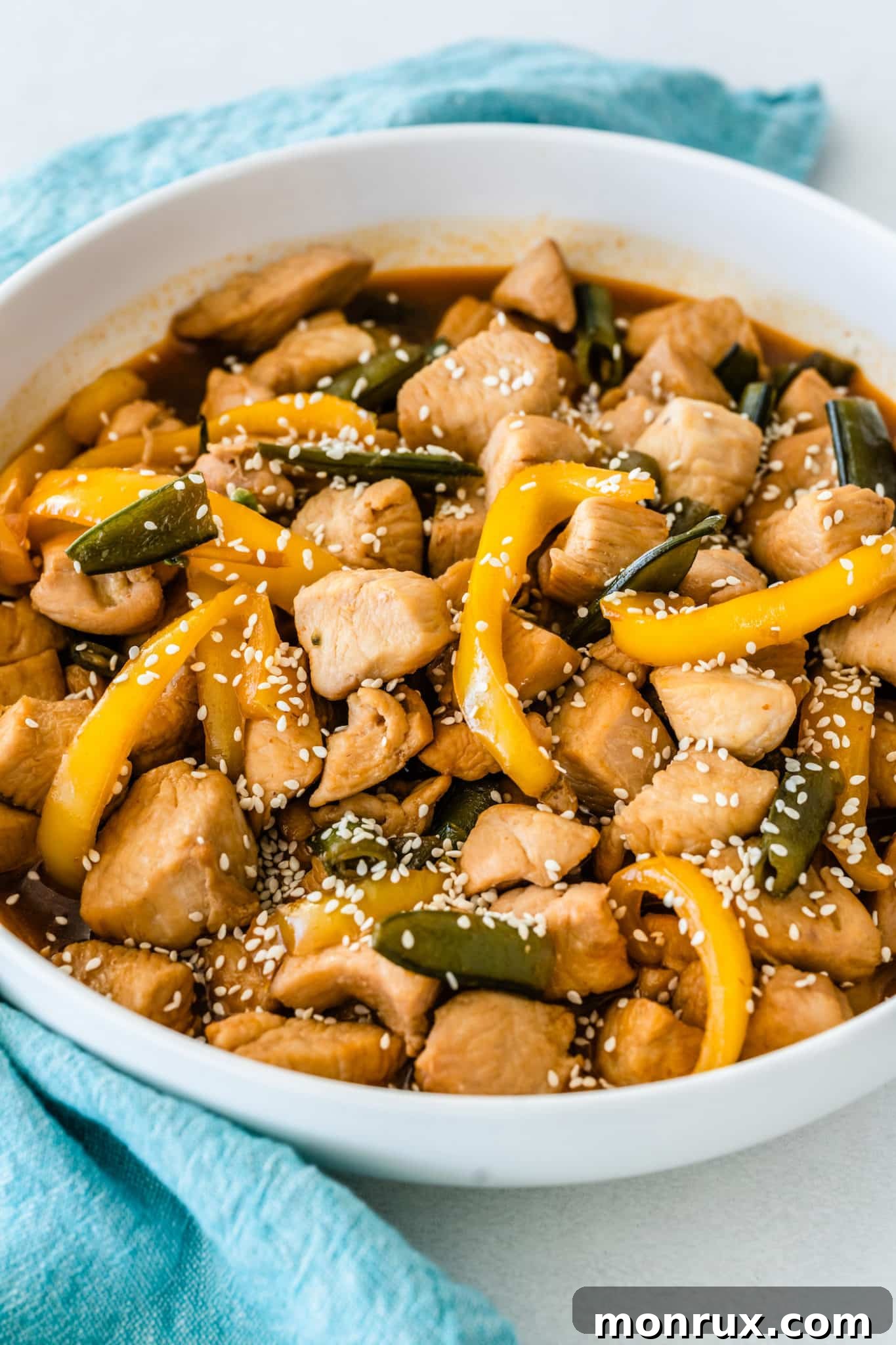 A beautifully plated bowl of honey sesame chicken with bell peppers and snap peas, garnished with sesame seeds, ready to be enjoyed.