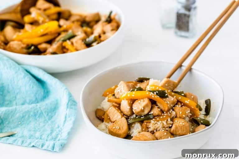 A bowl of honey sesame chicken with bell peppers and snap peas, garnished with sesame seeds.