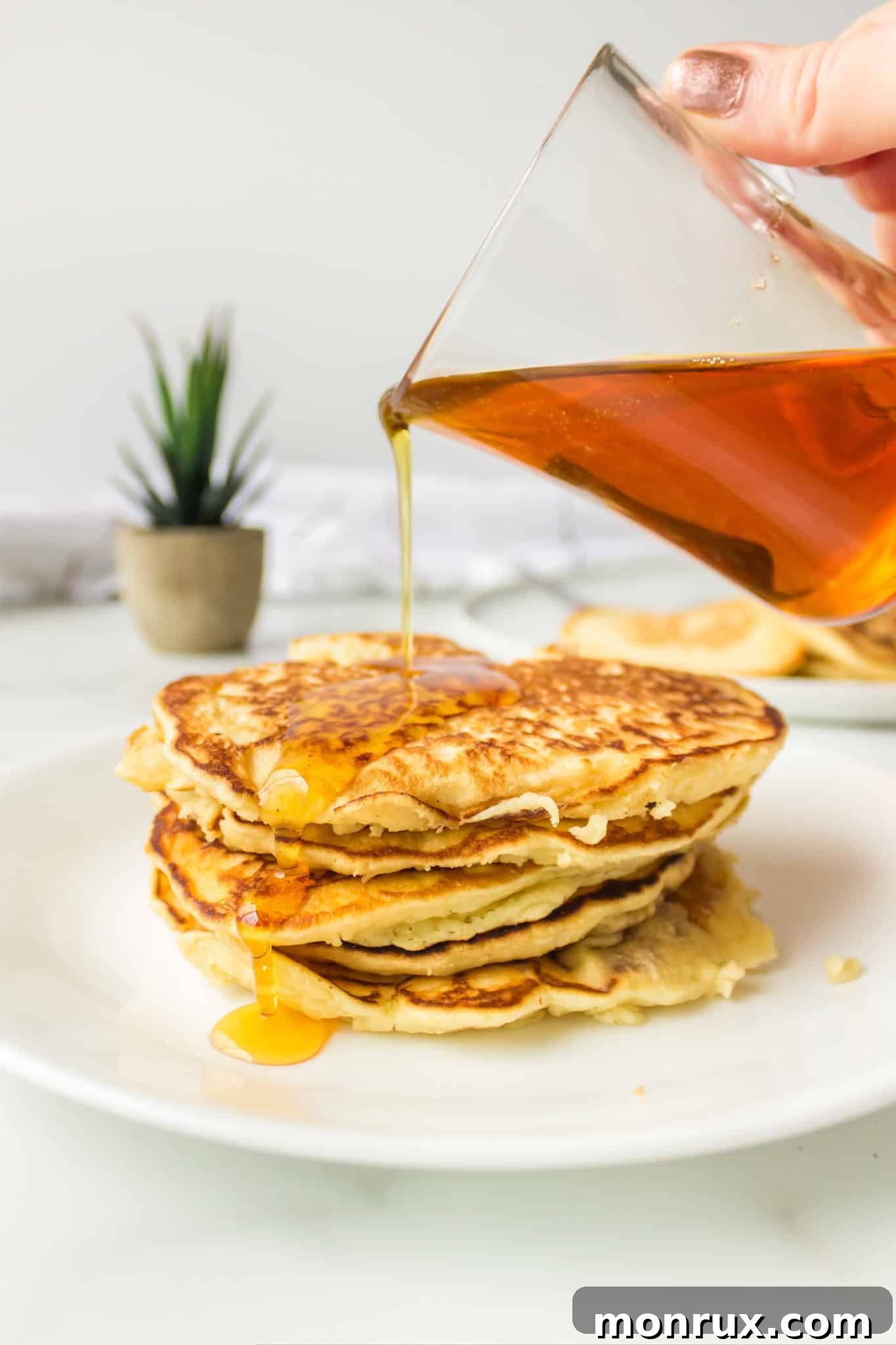 A stack of golden brown coconut milk pancakes drizzled with maple syrup and garnished with fresh berries.