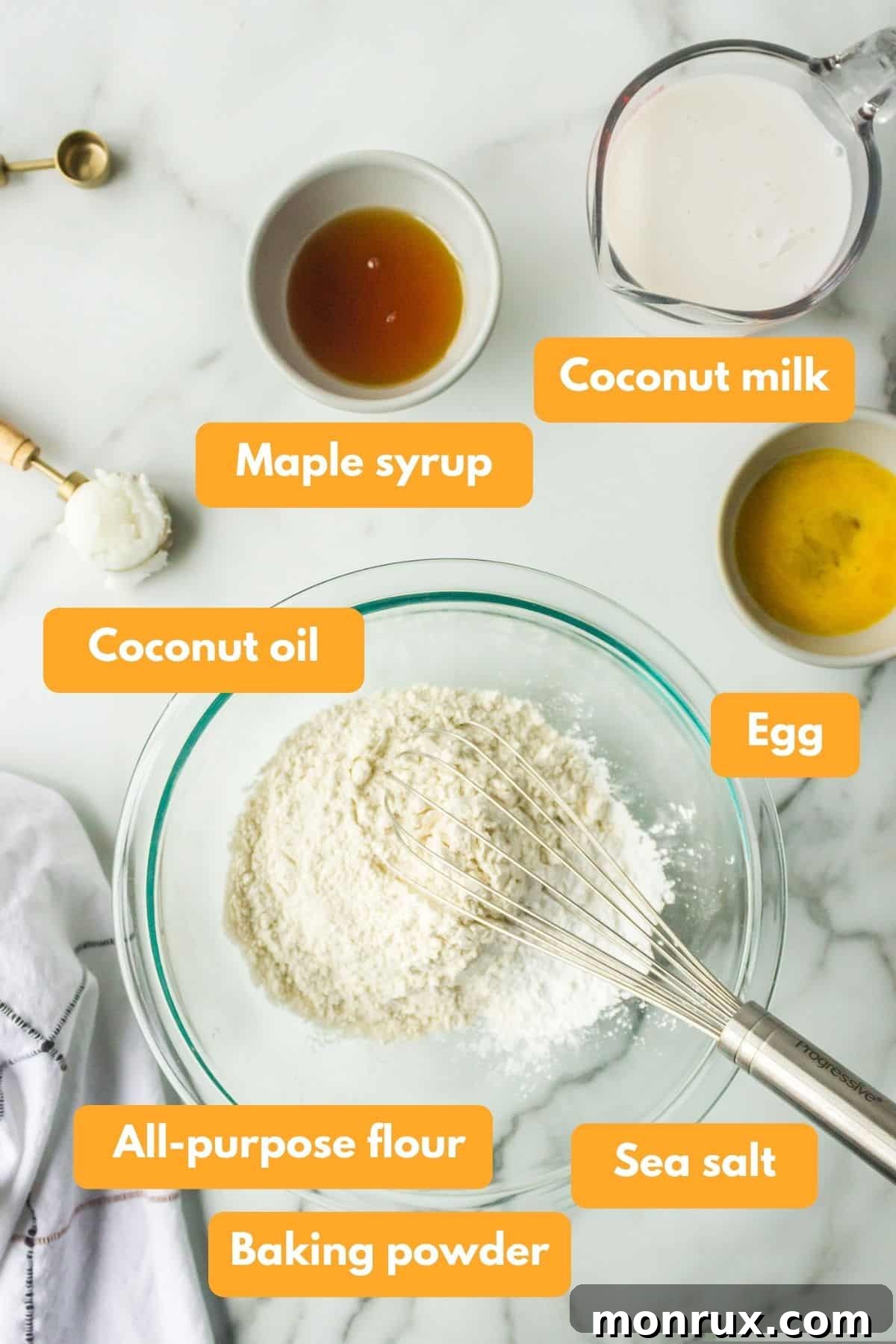 Essential ingredients laid out for making coconut milk pancakes, including flour, coconut milk, egg, and maple syrup.