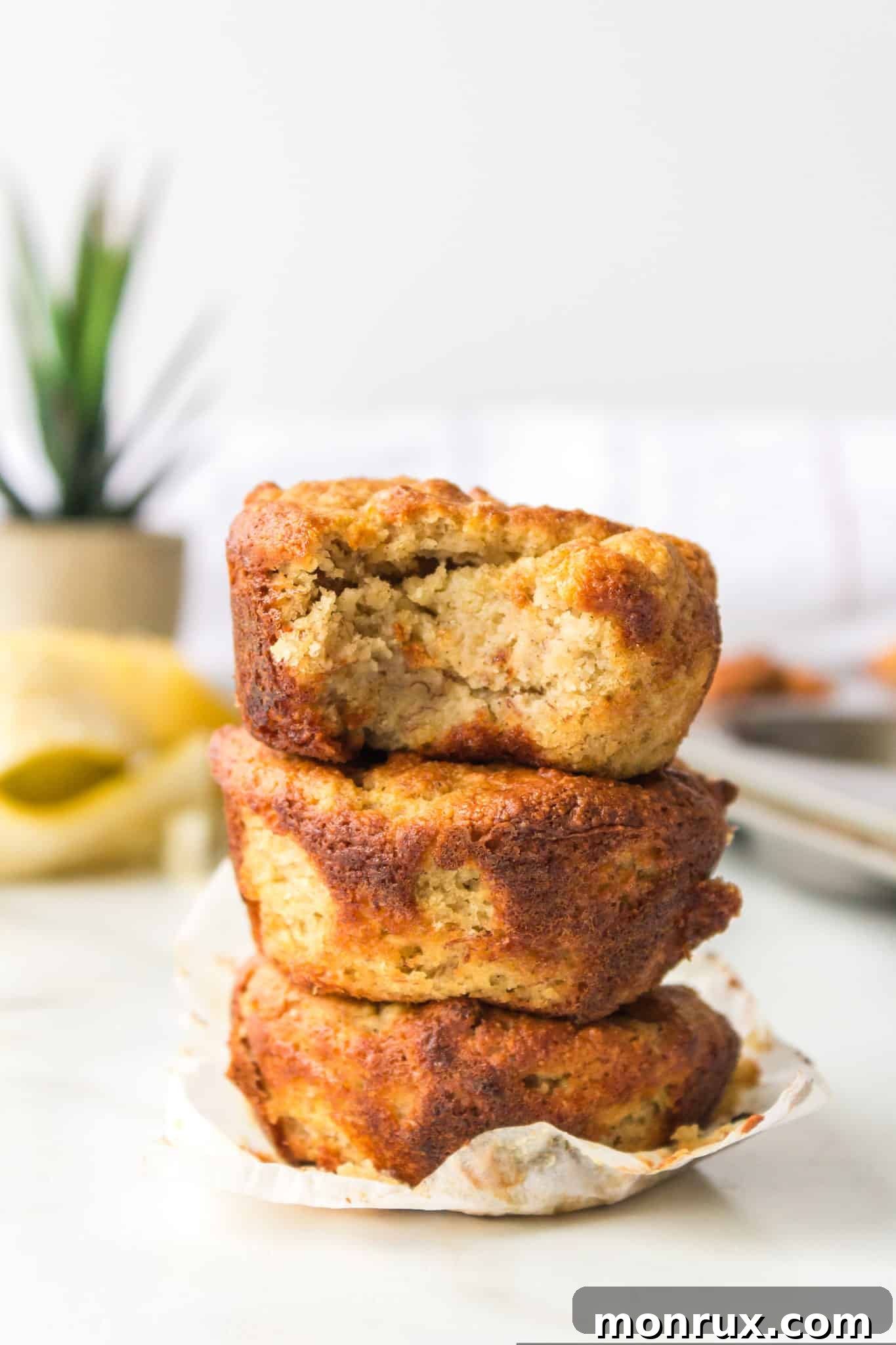 Three almond flour banana muffins stacked together on a rustic wooden surface, highlighting their golden-brown tops and moist interior.