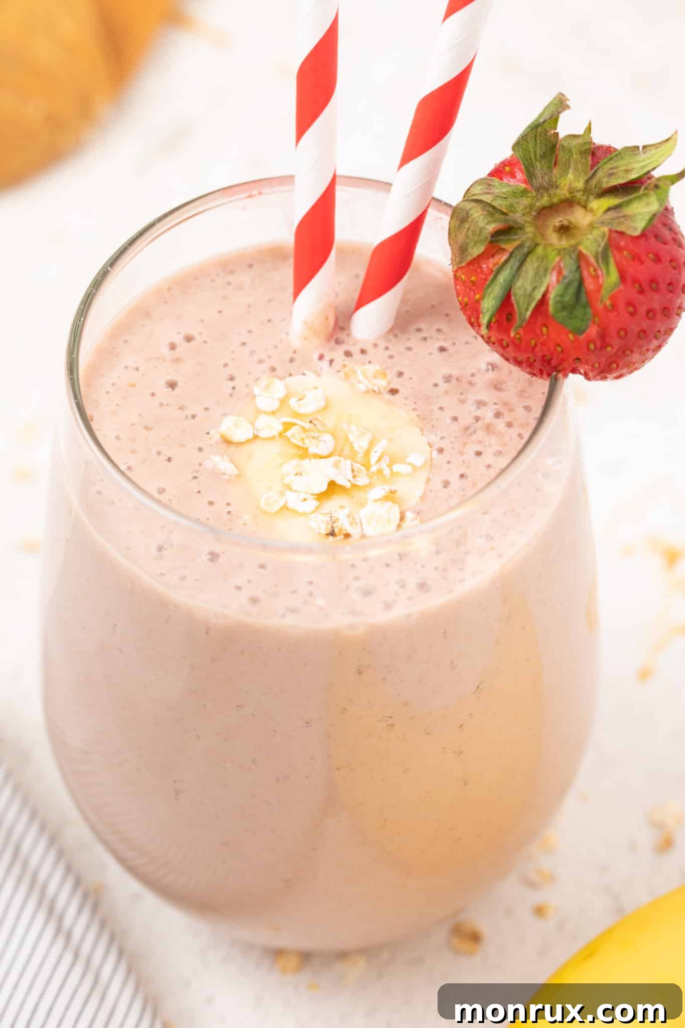 Vibrant oat milk strawberry banana smoothie served in a tall glass, garnished with fresh strawberries.