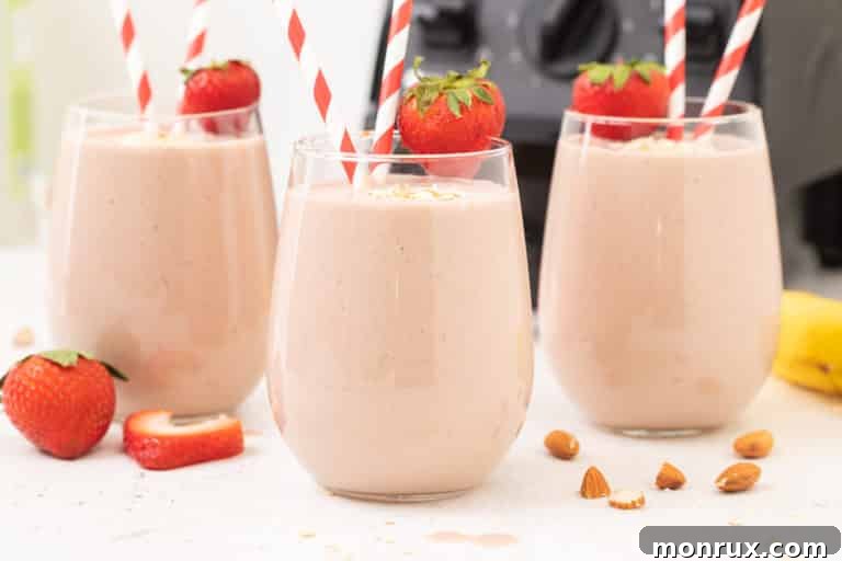 Two glasses of strawberry smoothies garnished with fresh strawberries and basil leaves.