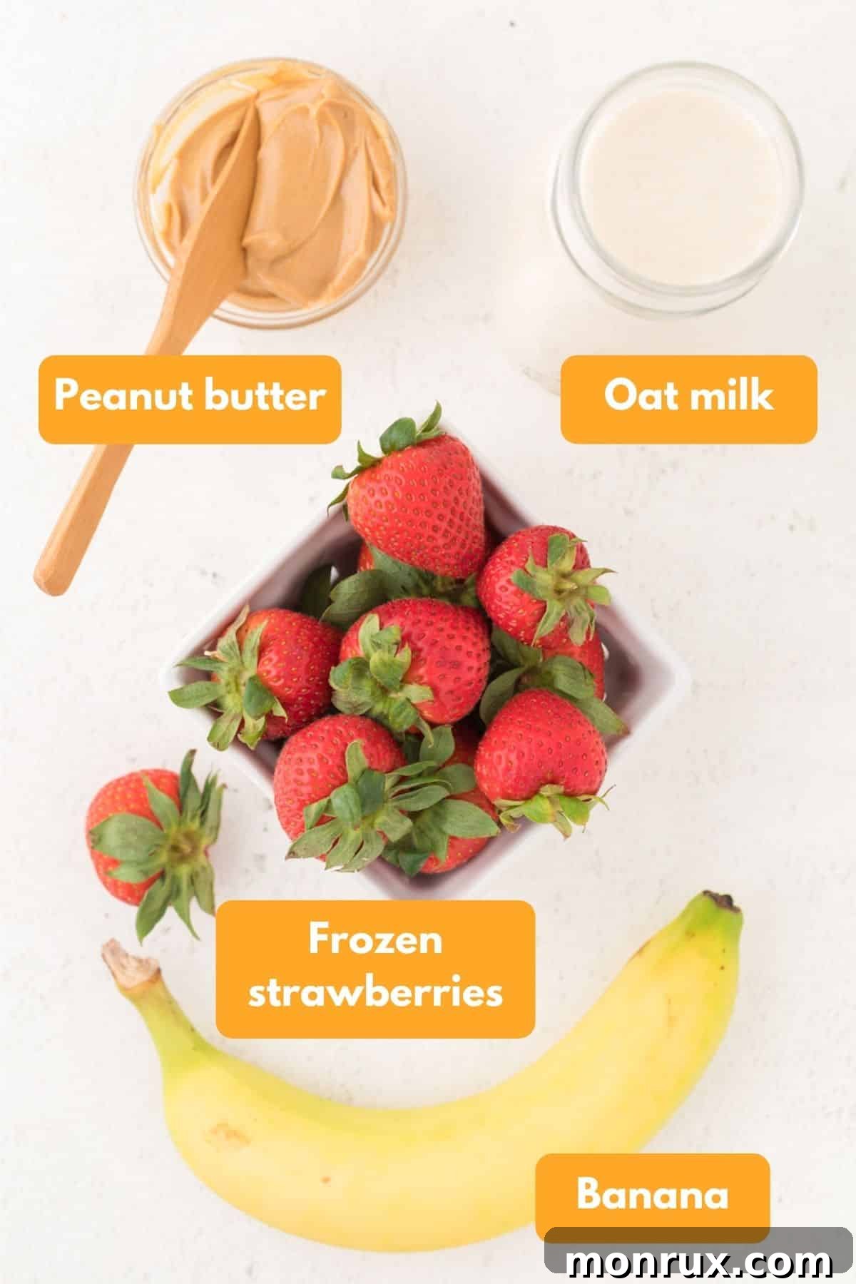 Assortment of fresh and frozen ingredients for a strawberry smoothie, including strawberries, bananas, peanut butter, and oat milk.