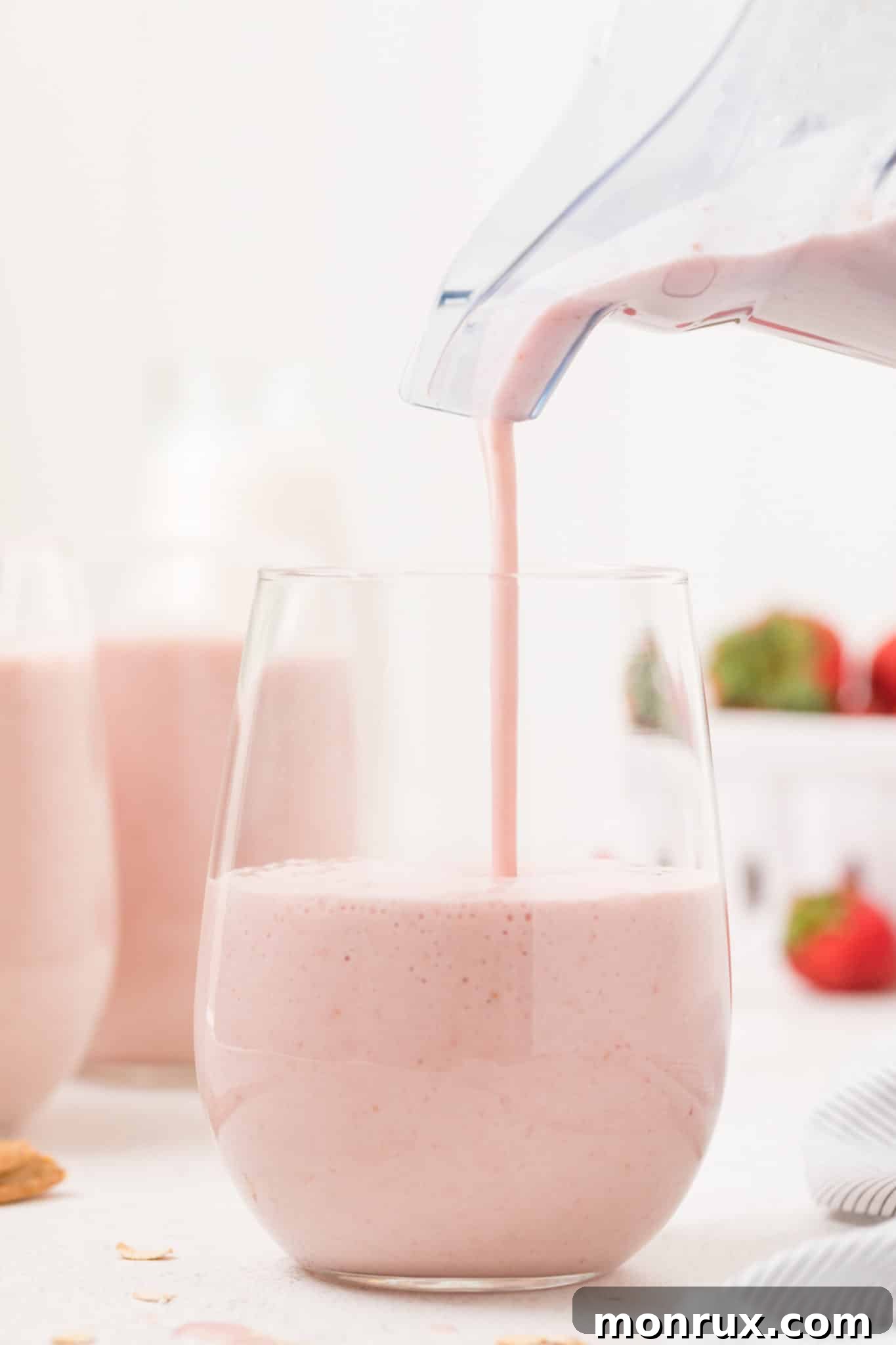 Freshly blended strawberry smoothie being poured into a clear glass, showing its creamy texture.