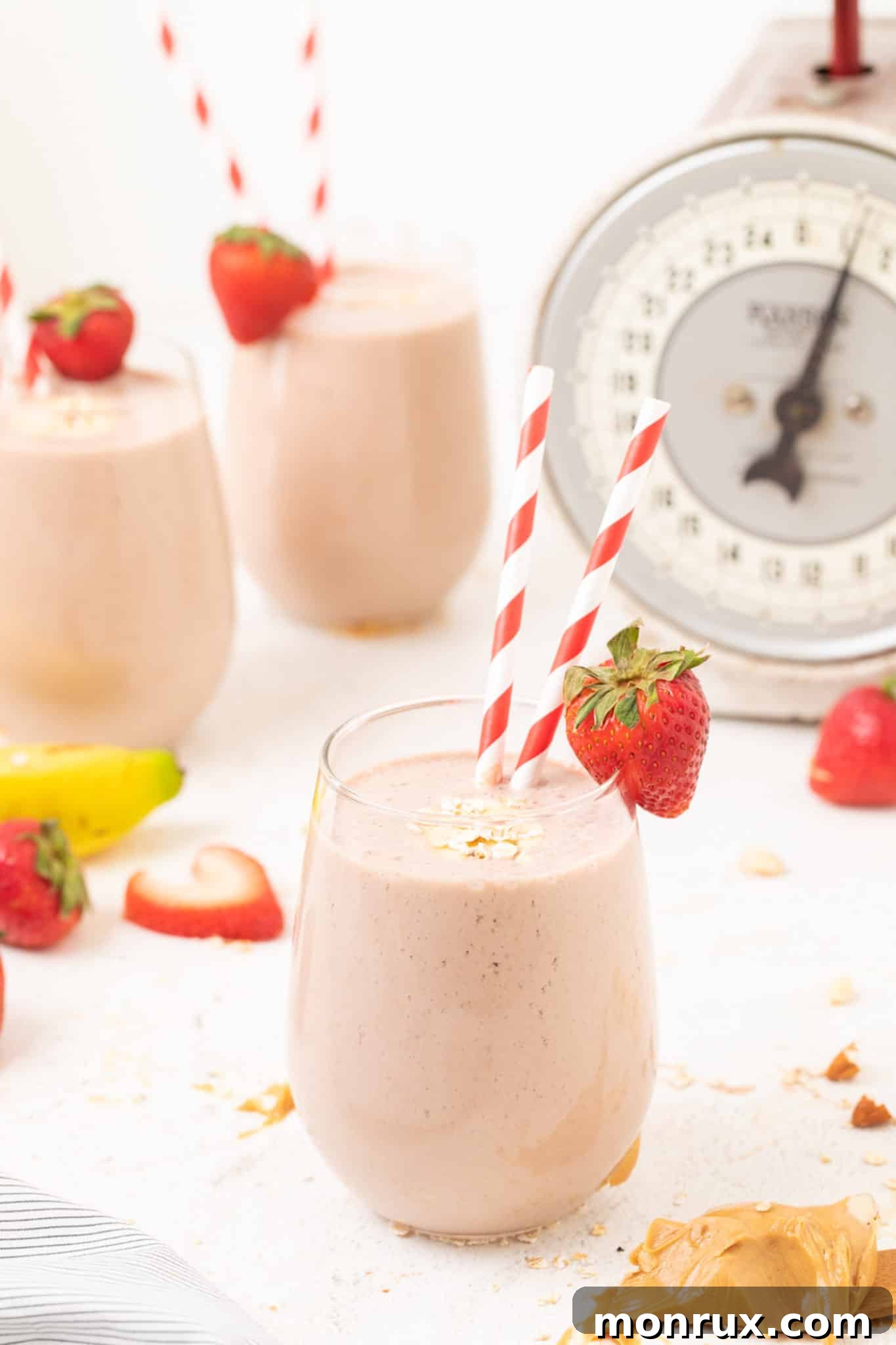 Three glasses of creamy strawberry smoothie, each with a straw, ready to be enjoyed.