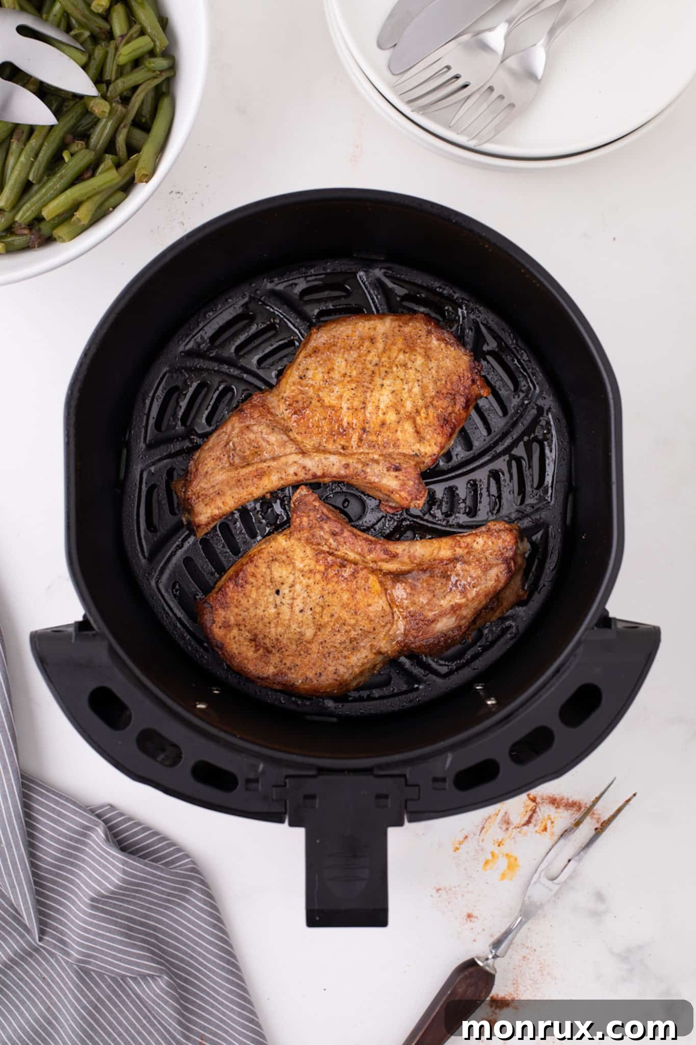 Cooked pork chops with no breading in an air fryer, served with green beans.