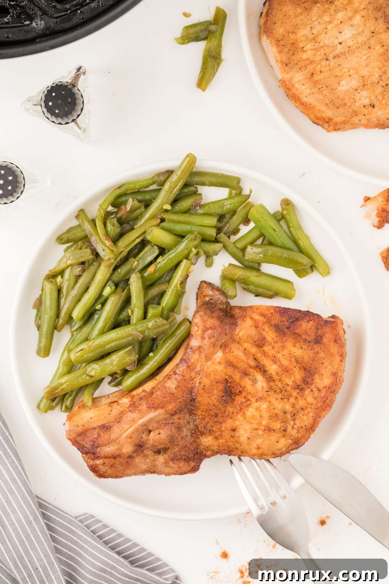 Cooked air fryer pork chops served on a plate with fresh green beans.