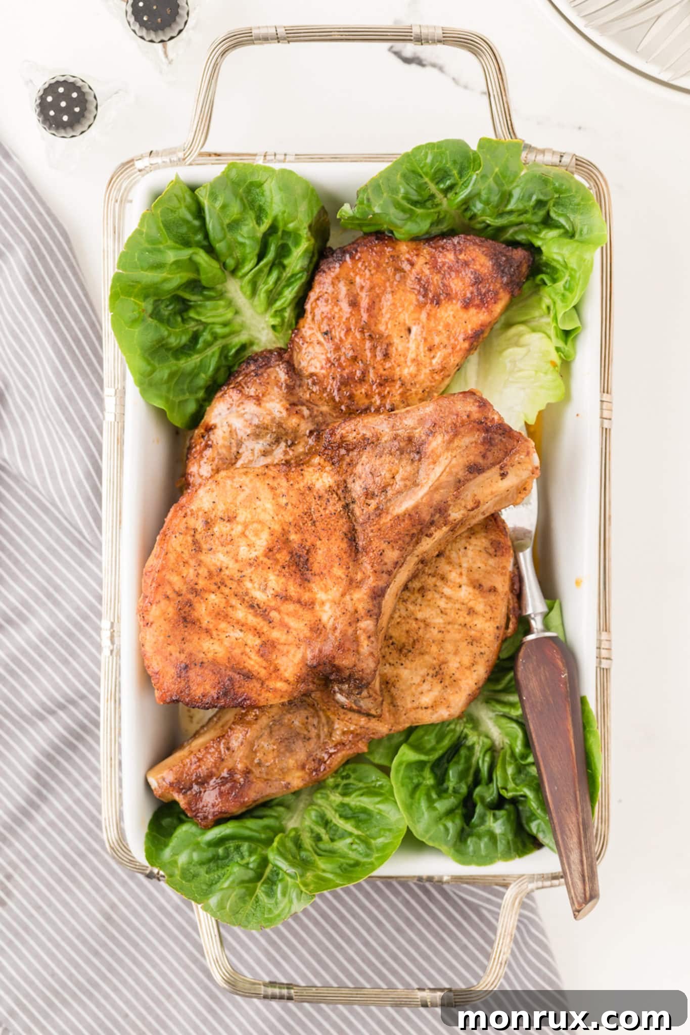Cooked air fryer pork chops arranged on a serving dish with fresh lettuce garnish.