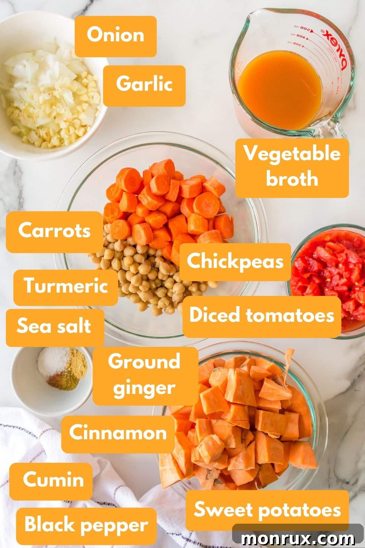 A carefully arranged display of fresh ingredients for instant pot chickpea stew, including chickpeas, sweet potatoes, carrots, onions, and spices.