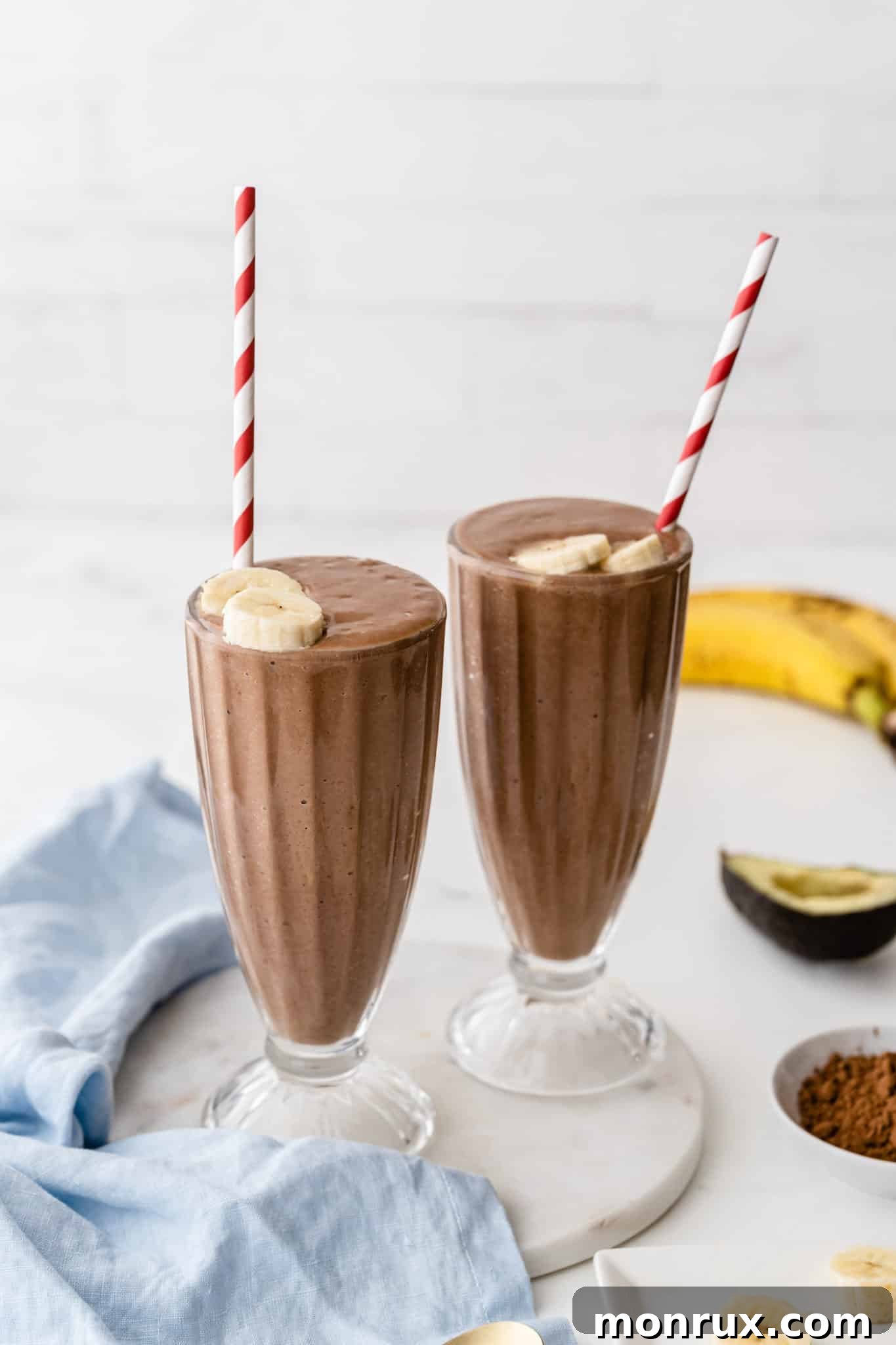 Chocolate avocado smoothies served in two milkshake glasses with straws, garnished with chocolate shavings.