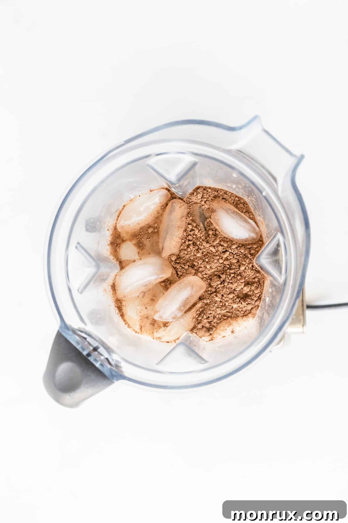 Cocoa powder, avocado, and ice in a blender to make chocolate avocado smoothie.