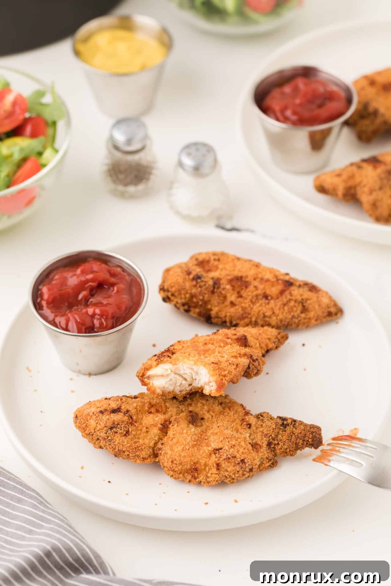Plate of golden-brown air fryer chicken tenders with ketchup and a fork, ready to be enjoyed.