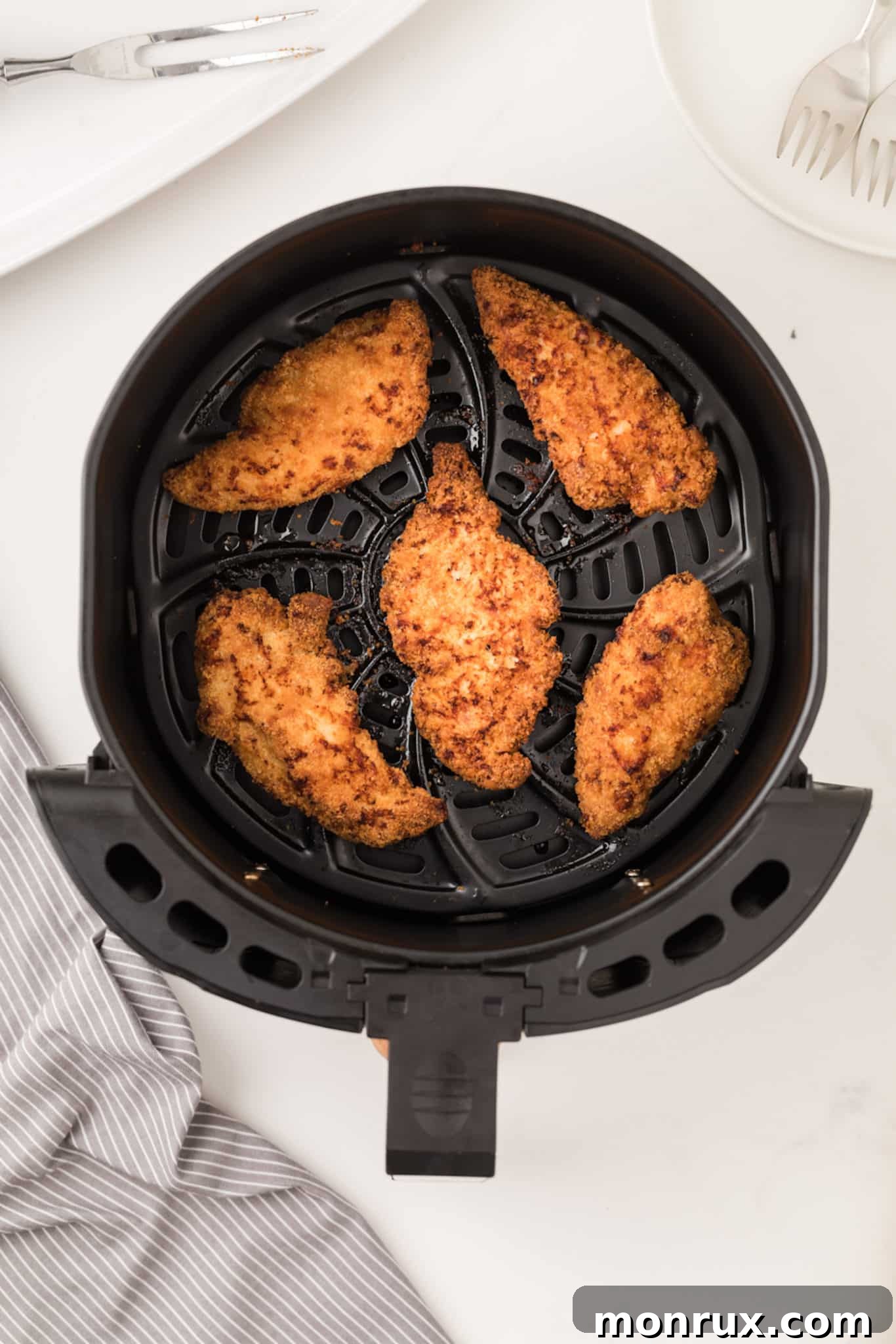 Cooked, golden-brown breaded chicken tenders inside an air fryer basket, ready to be removed.