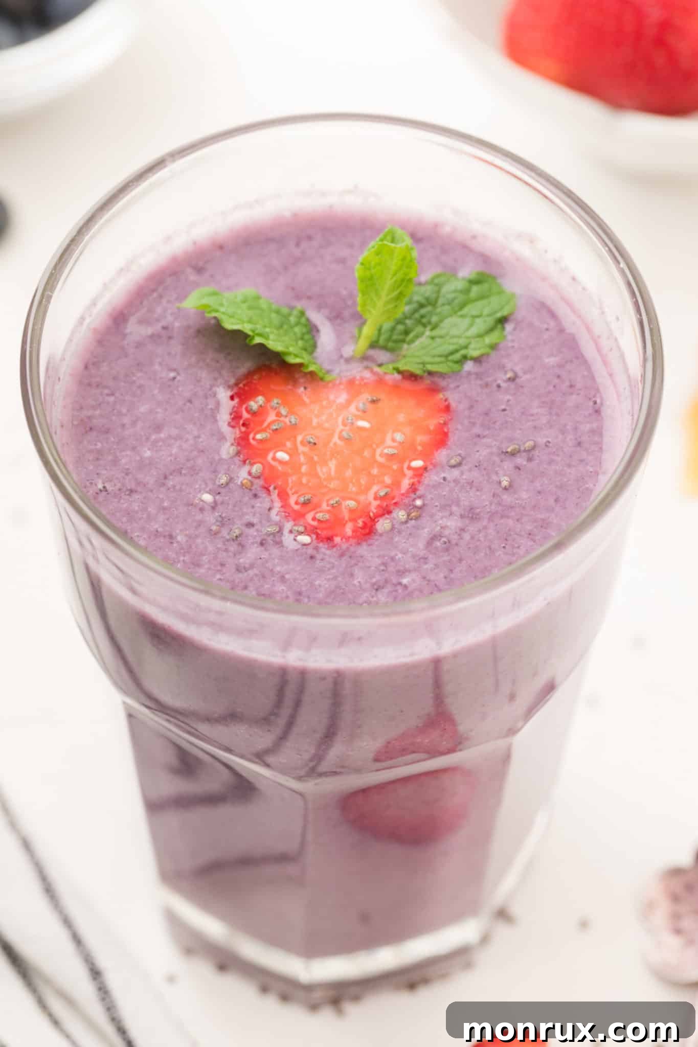 A vibrant strawberry and blueberry smoothie served in a clear glass with a straw.