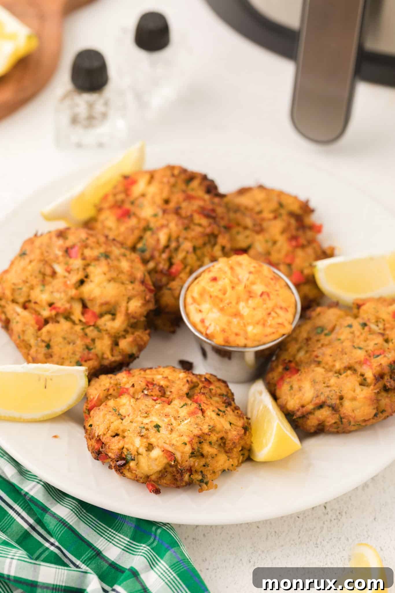 A beautifully arranged serving plate with cooked crab cakes, fresh lemon slices, and a small bowl of dipping sauce.