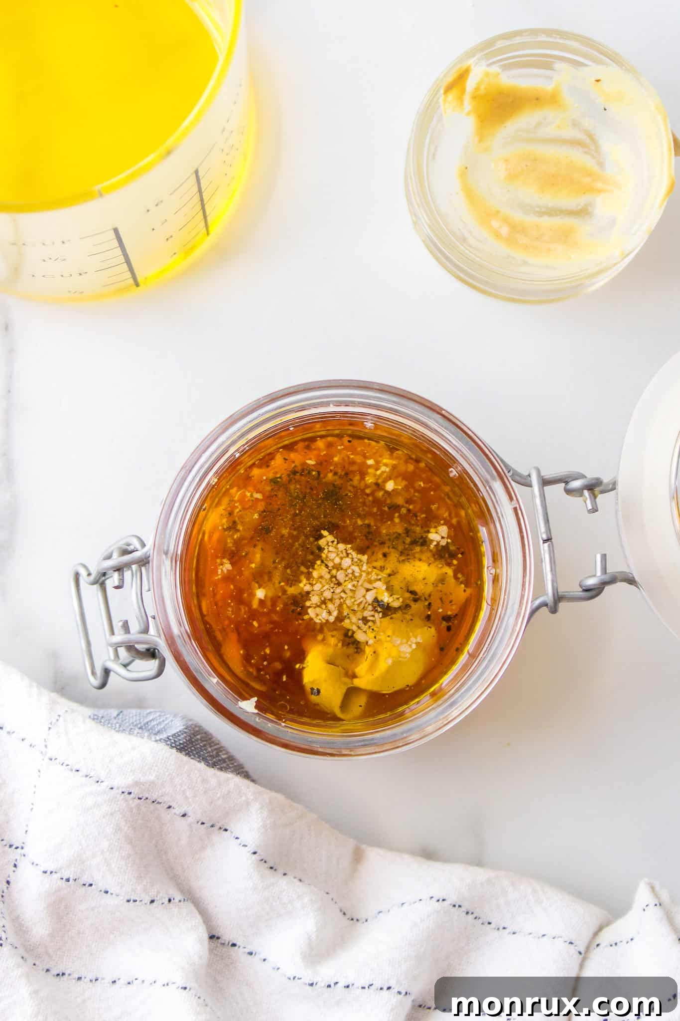 A clear glass jar with a flip-top lid, filled with the homemade Dijon mustard dressing ingredients, ready for shaking.