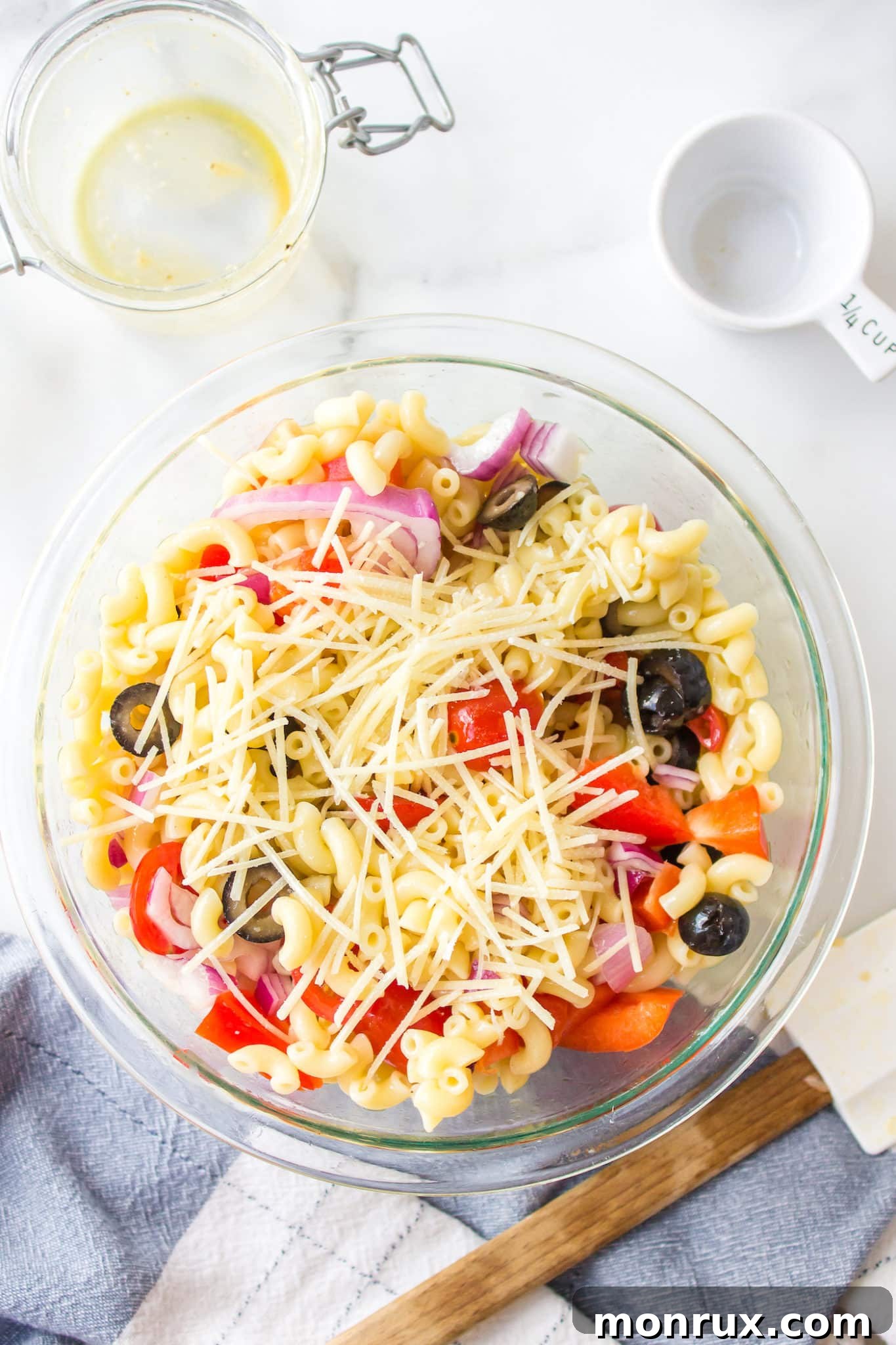 Top-down view of a large glass mixing bowl brimming with colorful pasta salad, generously topped with shredded Parmesan cheese.