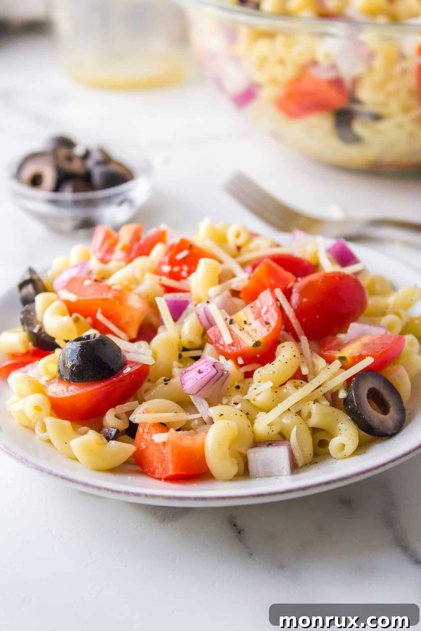 Side view of a serving of gluten-free pasta salad on a white plate, garnished with fresh tomatoes and black olives, showcasing its vibrant ingredients.