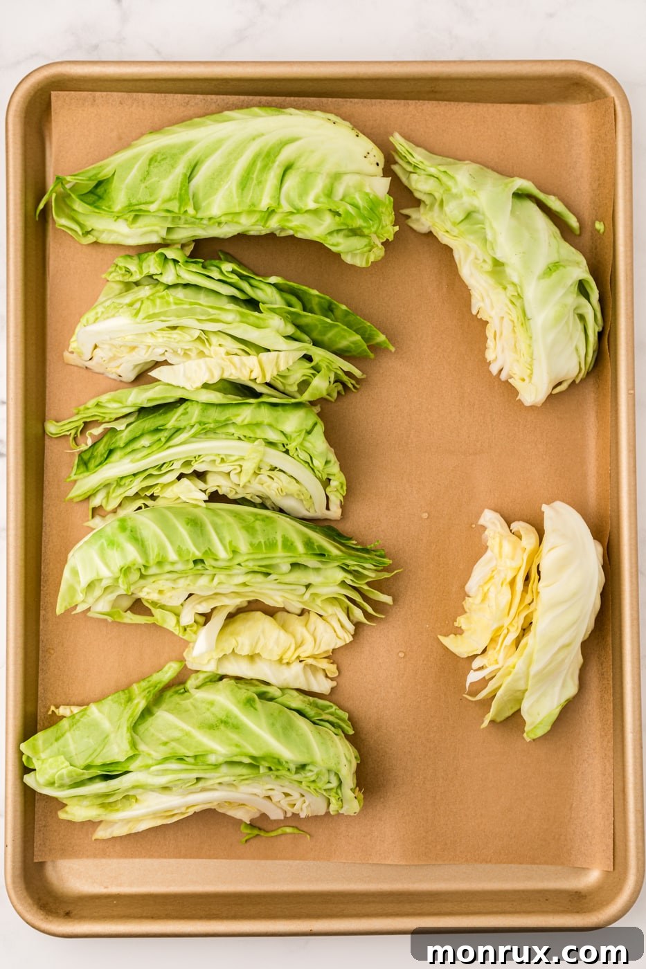 Blanched cabbage wedges laid out on a baking sheet lined with parchment paper, ready to be flash-frozen.