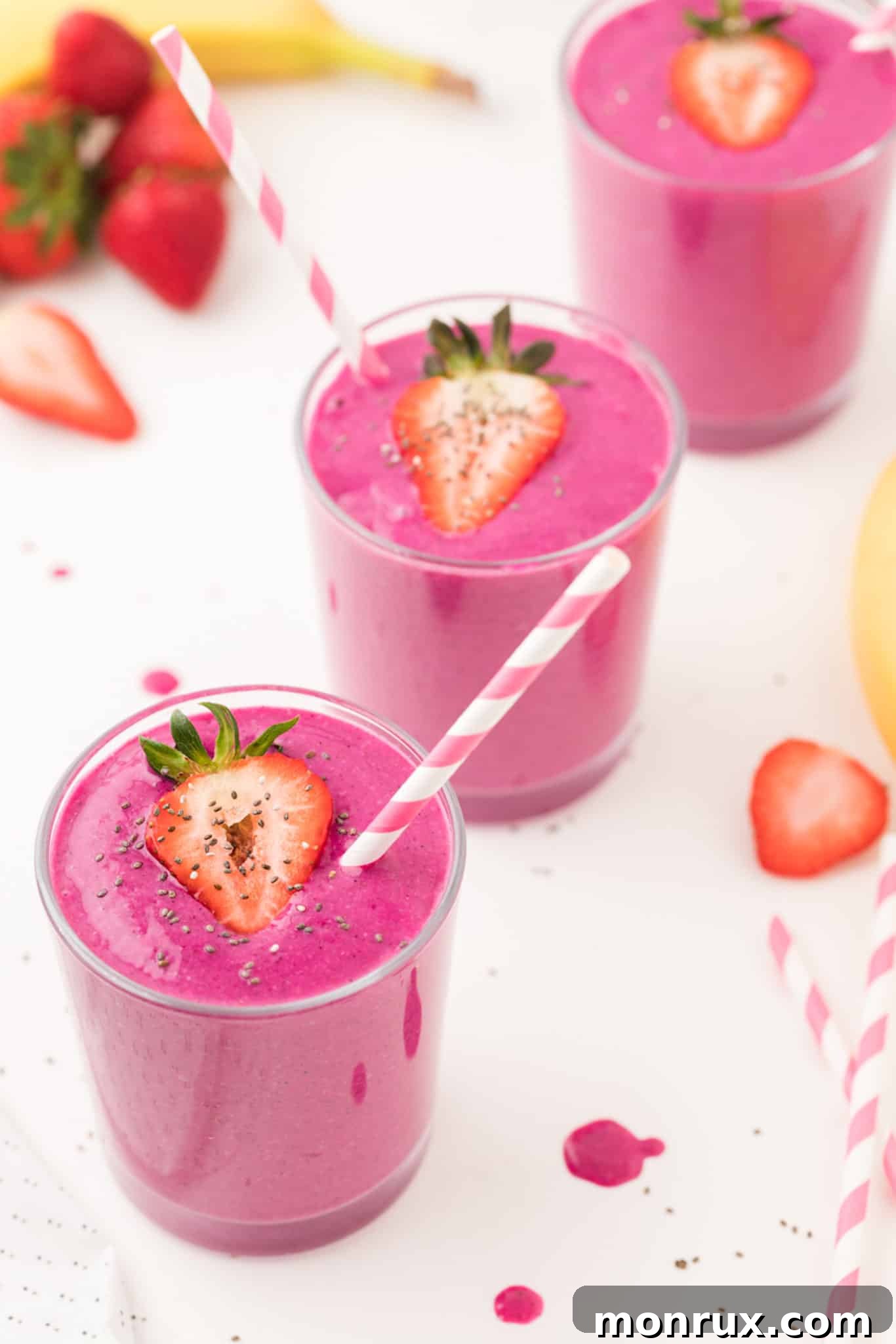Two glasses of purple dragon fruit smoothies with pink striped straws, garnished with fresh dragon fruit slices.